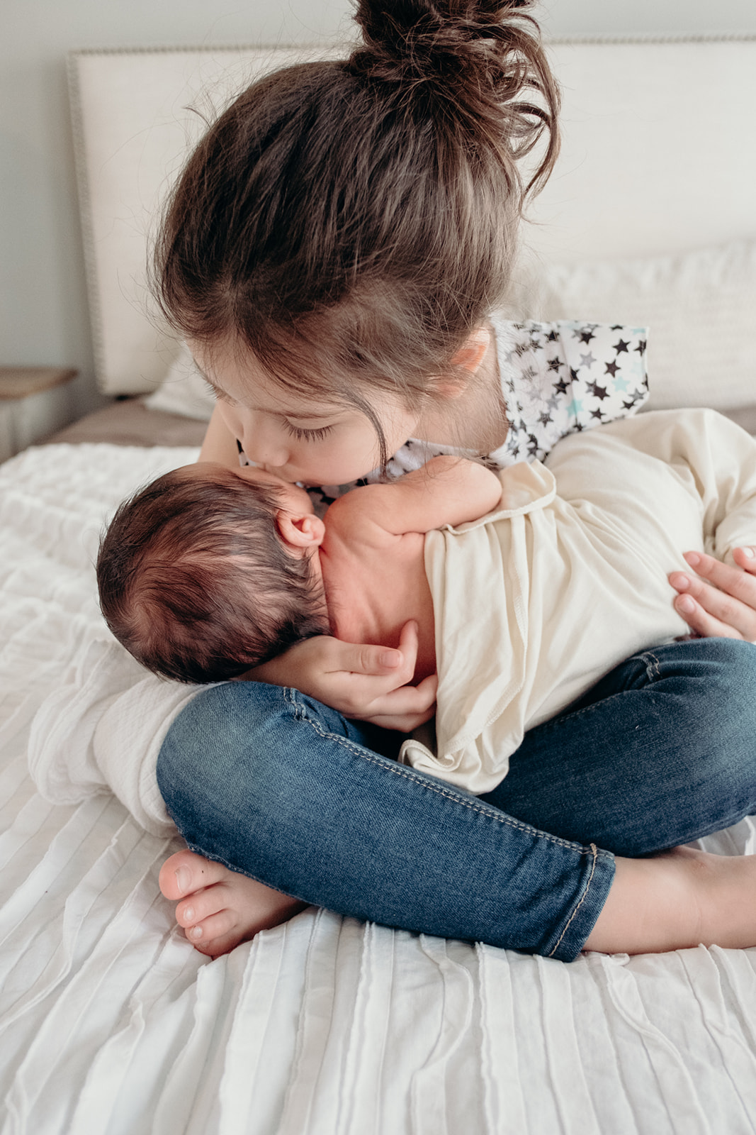 A little girl kisses her baby brother while she holds him on her lap during an in-home family photography session. 