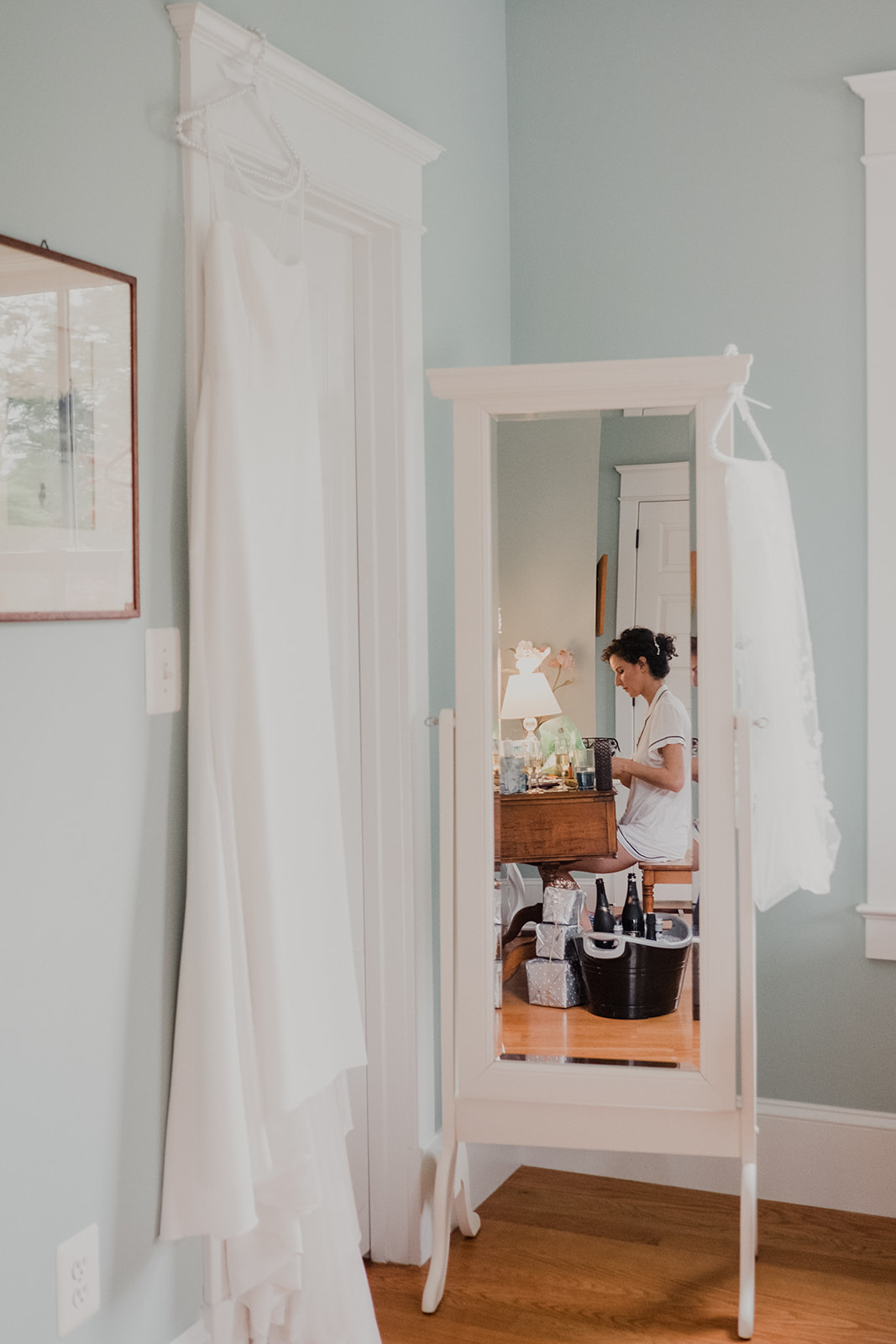 A brides reflection appears in a mirror that sits next to her long white wedding dress and veil in the house at Blue Hill Farm in Waterford, VA.
