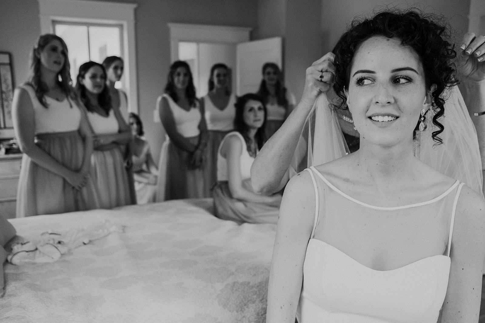 Bridesmaids look on while a bride gets her veil put in place before her outdoor wedding ceremony at Blue Hill Farm in Waterford, VA.