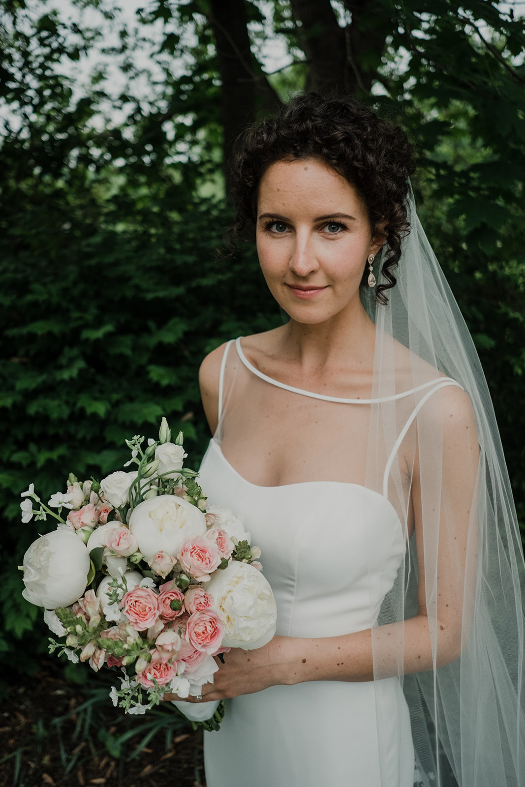  A bride holds a bouquet of pink and white and green florals before her outdoor wedding ceremony at Blue Hill Farm in Waterford, VA.