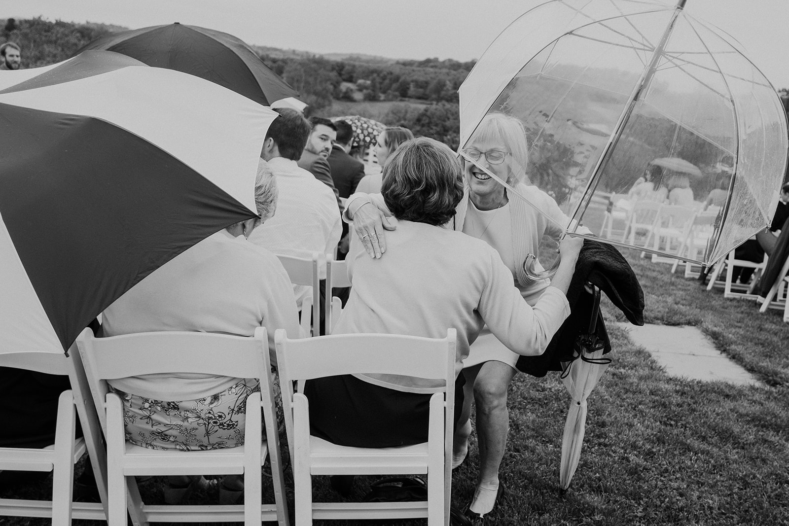 Guests hug under an umbrella at a spring outdoor wedding ceremony at Blue Hill Farm in Waterford, VA. 