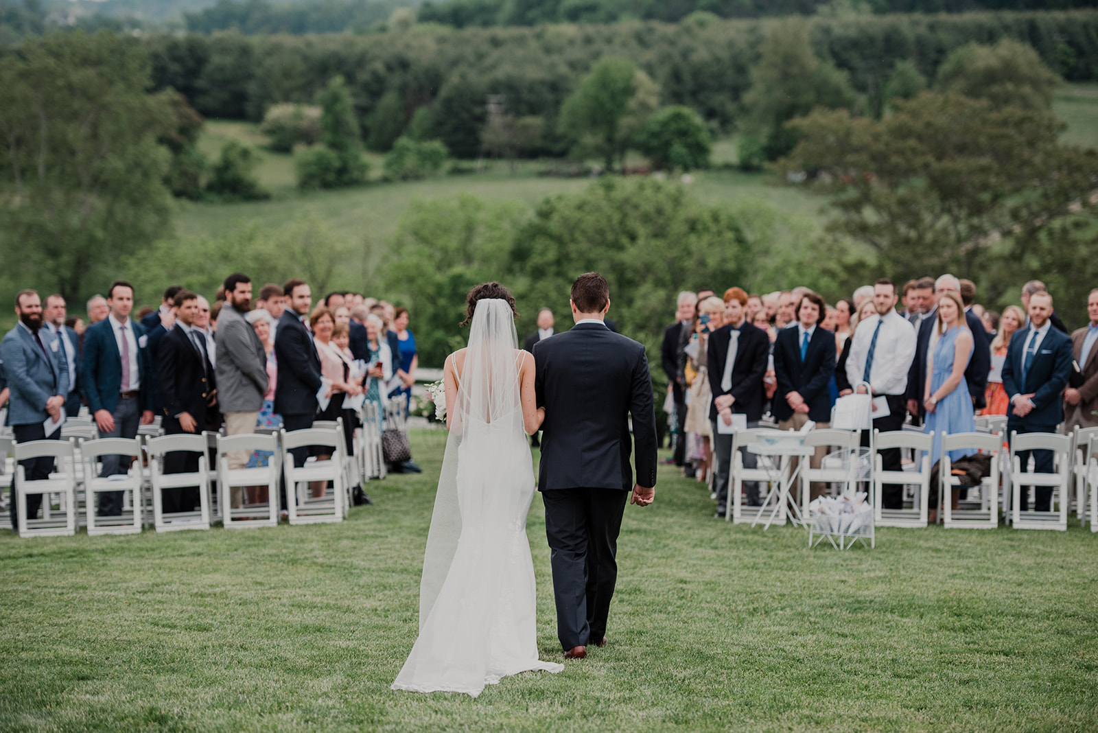 A bride is escorted by her brother to her outdoor wedding ceremony at Blue Hill Farm in Waterford, VA. 