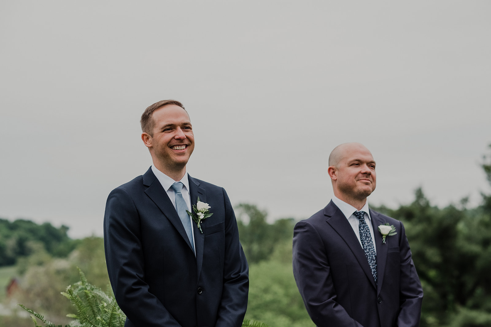 A groom smiles as he watches his bride walk down the aisle at their outdoor wedding ceremony at Blue Hill Farm in Waterford, VA. 