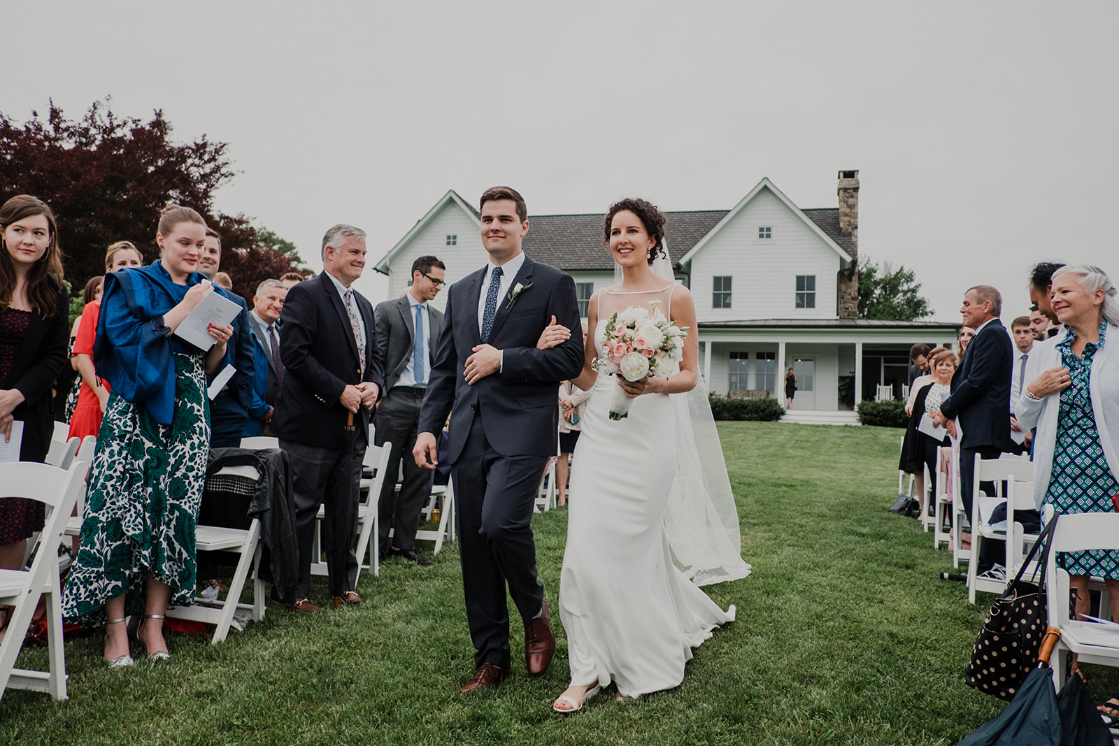 A bride is escorted by her brother down the aisle of her outdoor wedding at Blue Hill Farm in Waterford, VA.