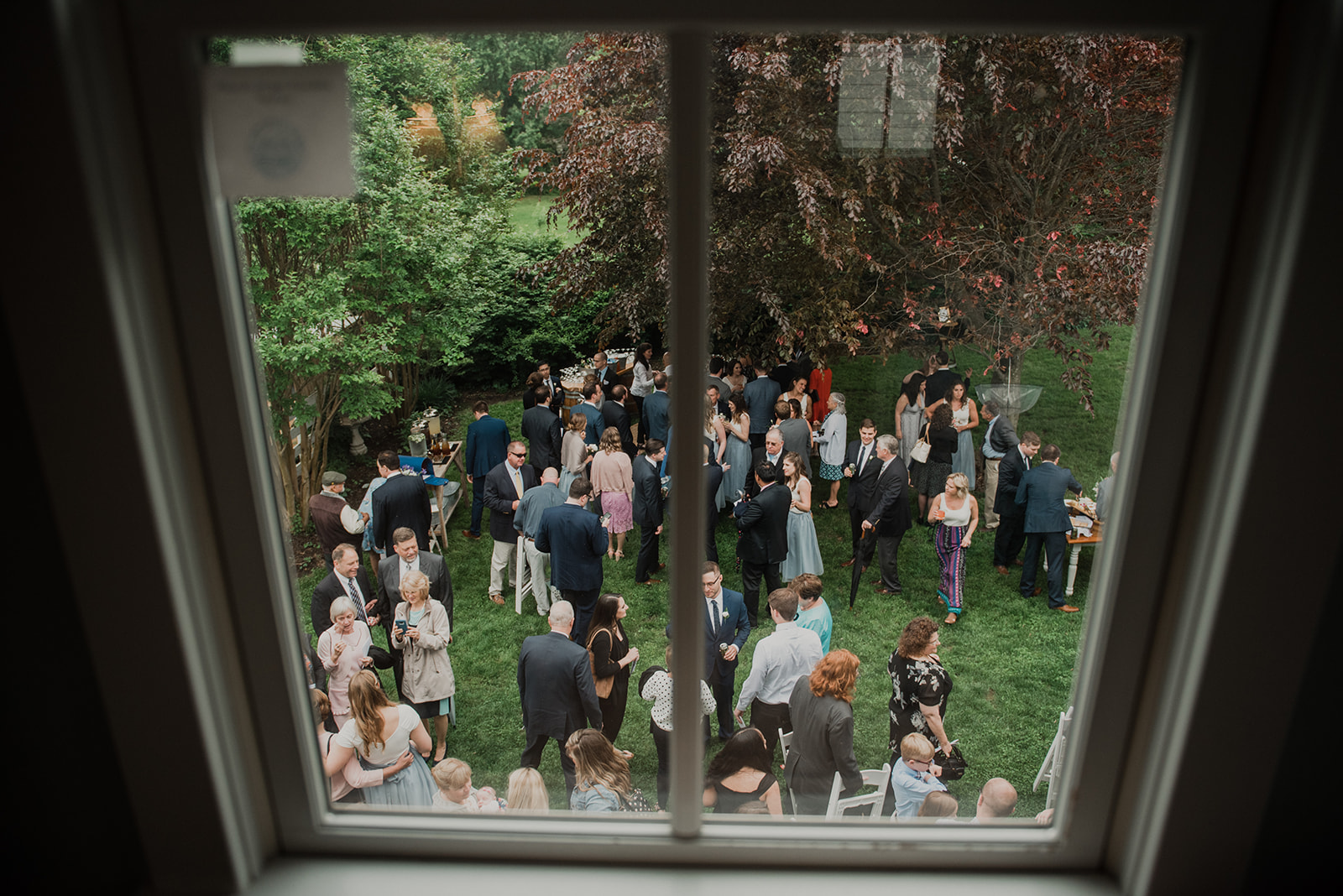 Guests are seen from above through a window enjoying cocktail hour at an outdoor wedding at Blue Hill Farm in Waterford, VA.