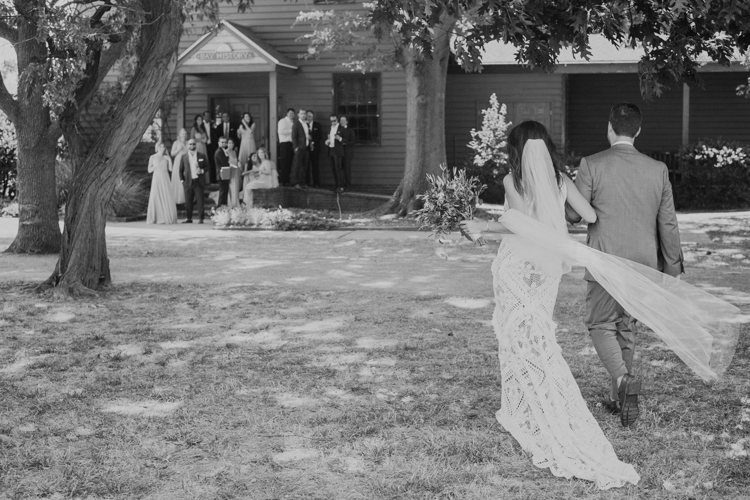 bride and groom walk towards wedding party after first look across a field