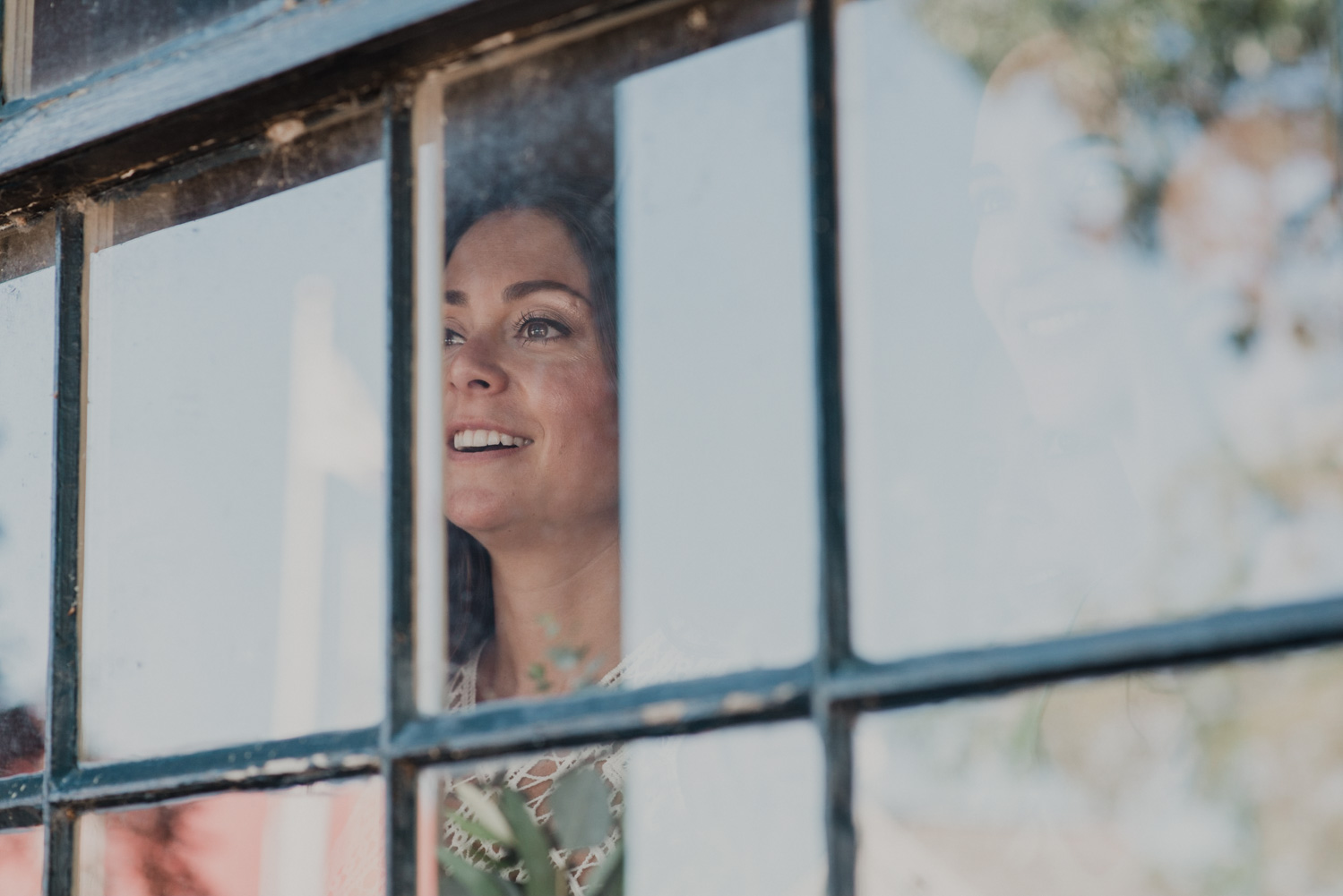 bride looks out window watching guests mingle before wedding