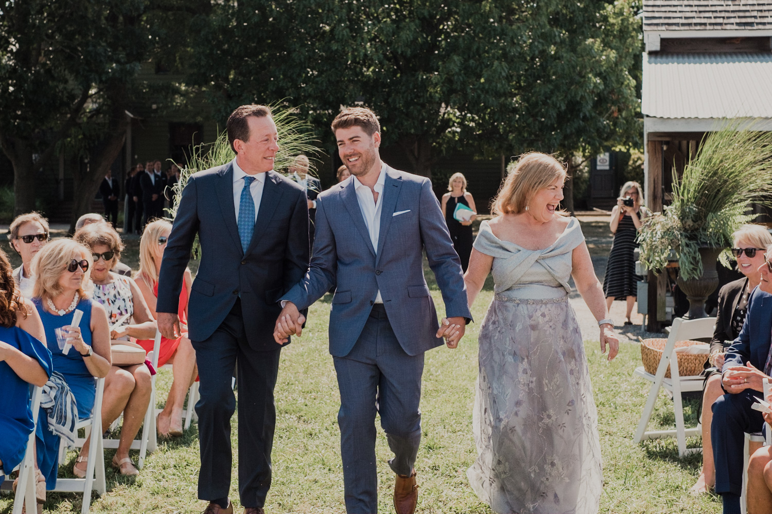 groom is escorted by both of his parents down the aisle at the start of wedding