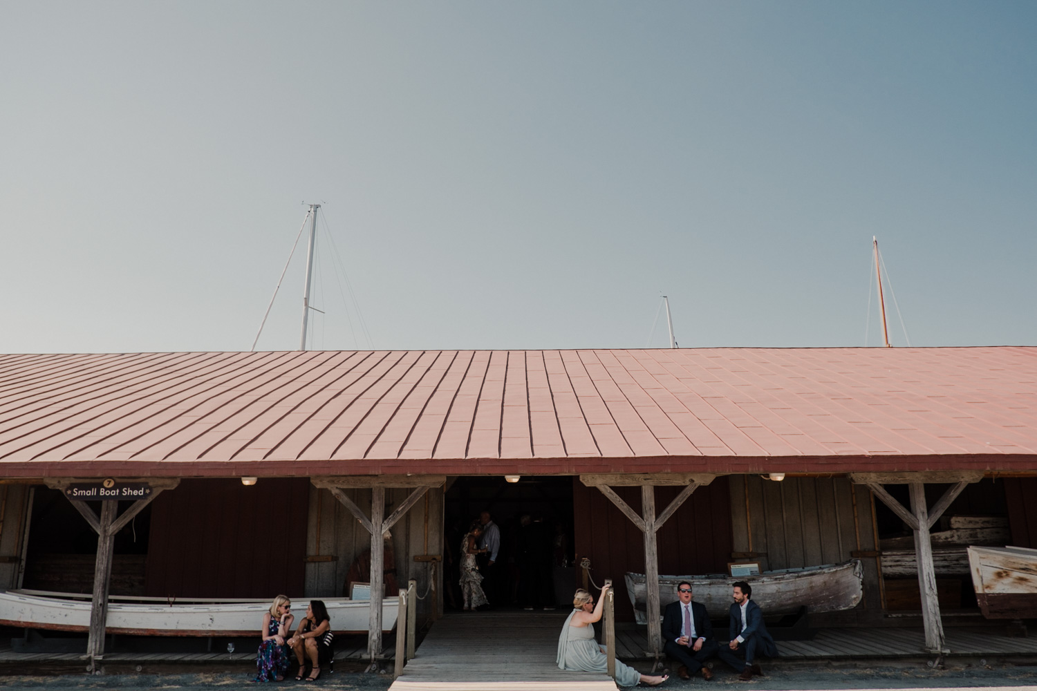 guests sit outside boat house during wedding cocktail hour at chesapeake bay maritime museum