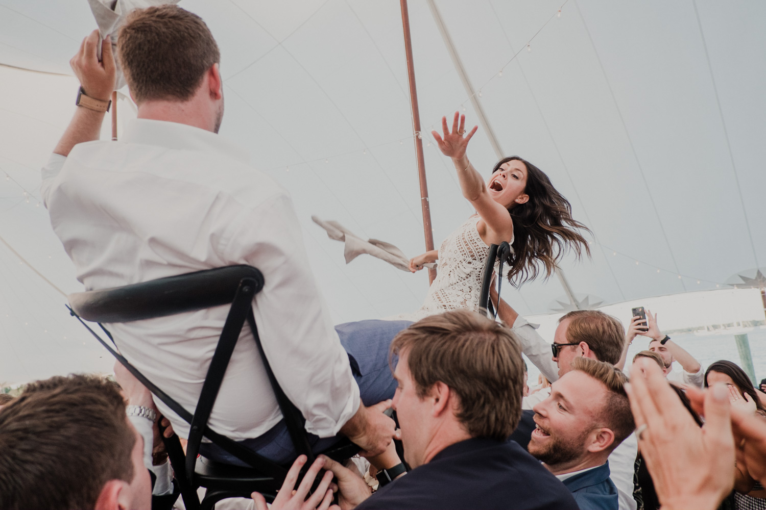 bride and groom reach for each other while lifted on chairs during the hora dance