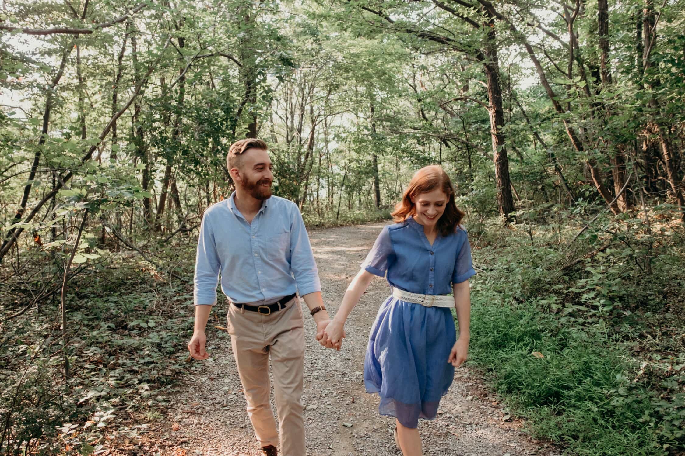 Sara and Marshall walking through the woods and holding hands at Bears Den Overlook