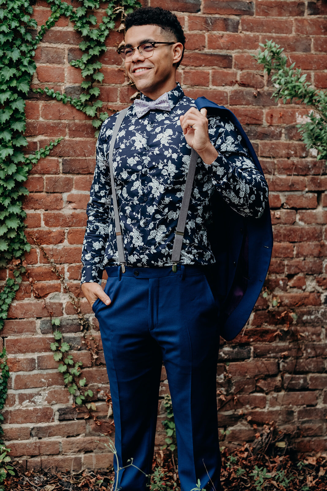 A bride in a sA groom in a floral shirt and bowtie poses next to an ivy wall in downtown Leesburg, VA.