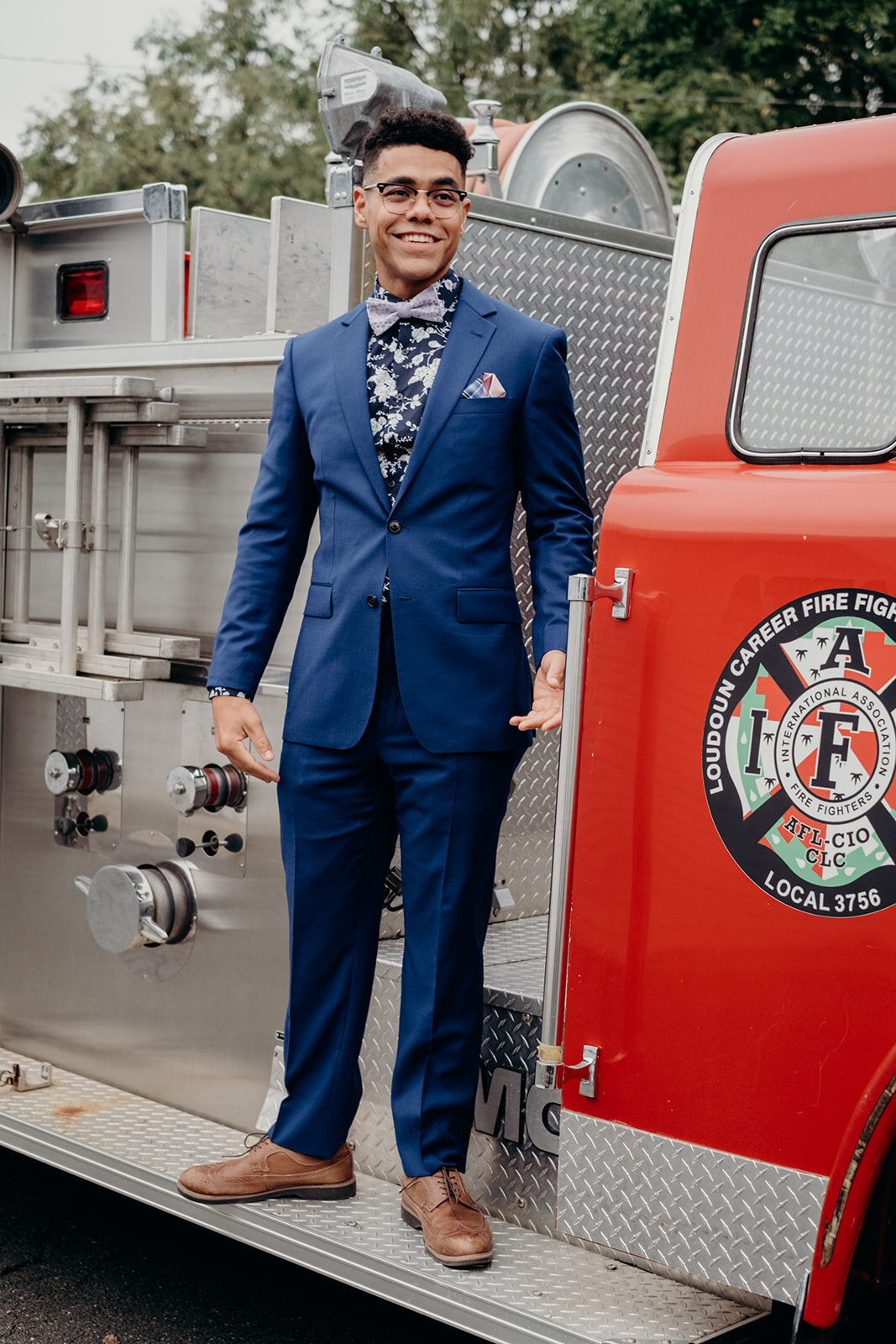 A groom stands on a firetruck as he prepares to walk down the aisle at his outdoor wedding ceremony at Birkby House in Leesburg, VA.