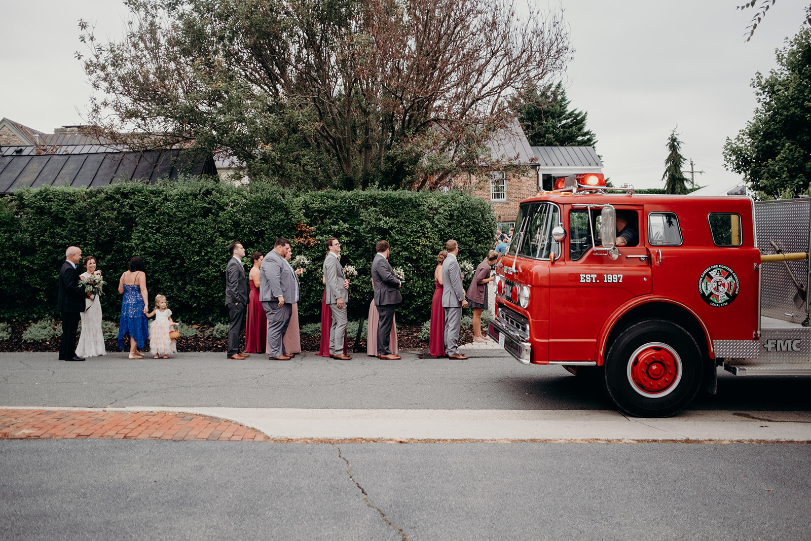 The wedding party stands next to a firetruck the groom rode into his wedding at Birkby House. 