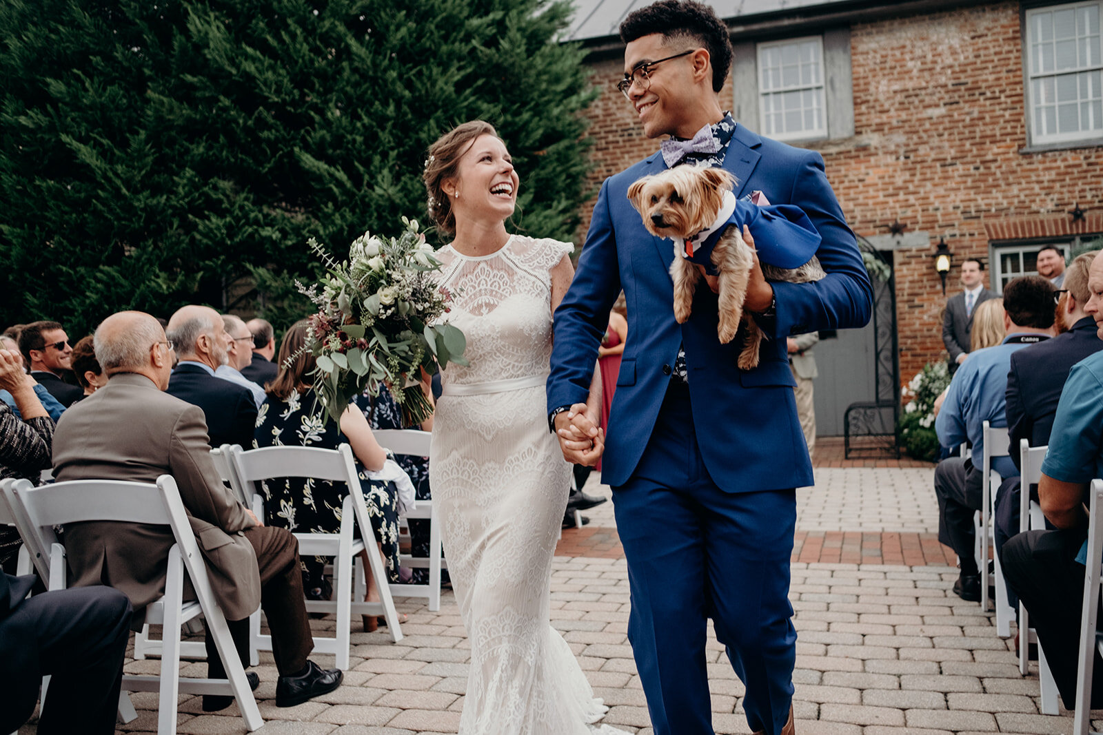 A bride and groom and their pup walk down the aisle at their outdoor wedding ceremony at Birkby House in Leesburg, VA. 