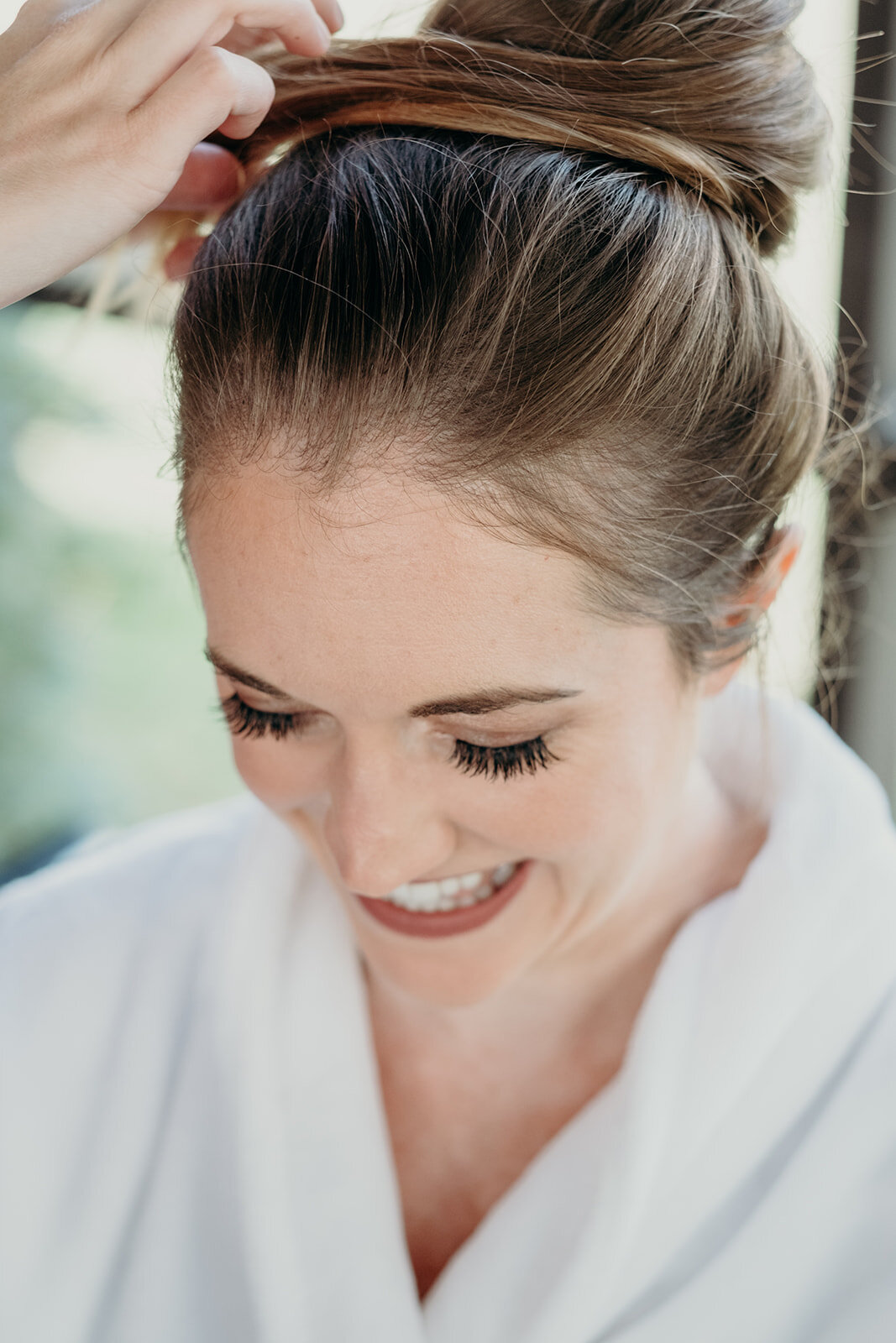A bride gets a high ballerina bun styled for her outdoor wedding ceremony. 