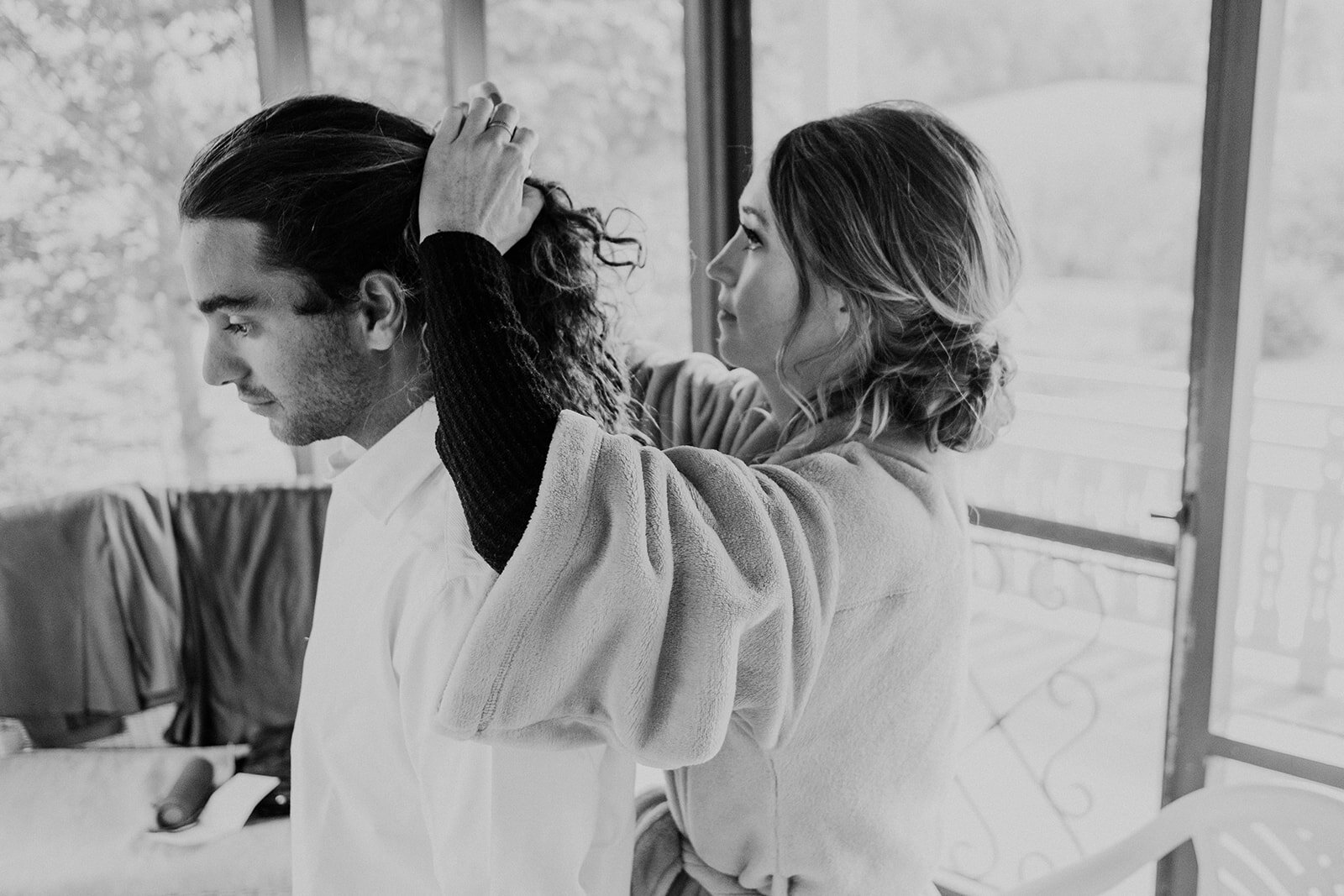 The sister of the bride helps her boyfriend do his hair before the outdoor farm wedding ceremony.
