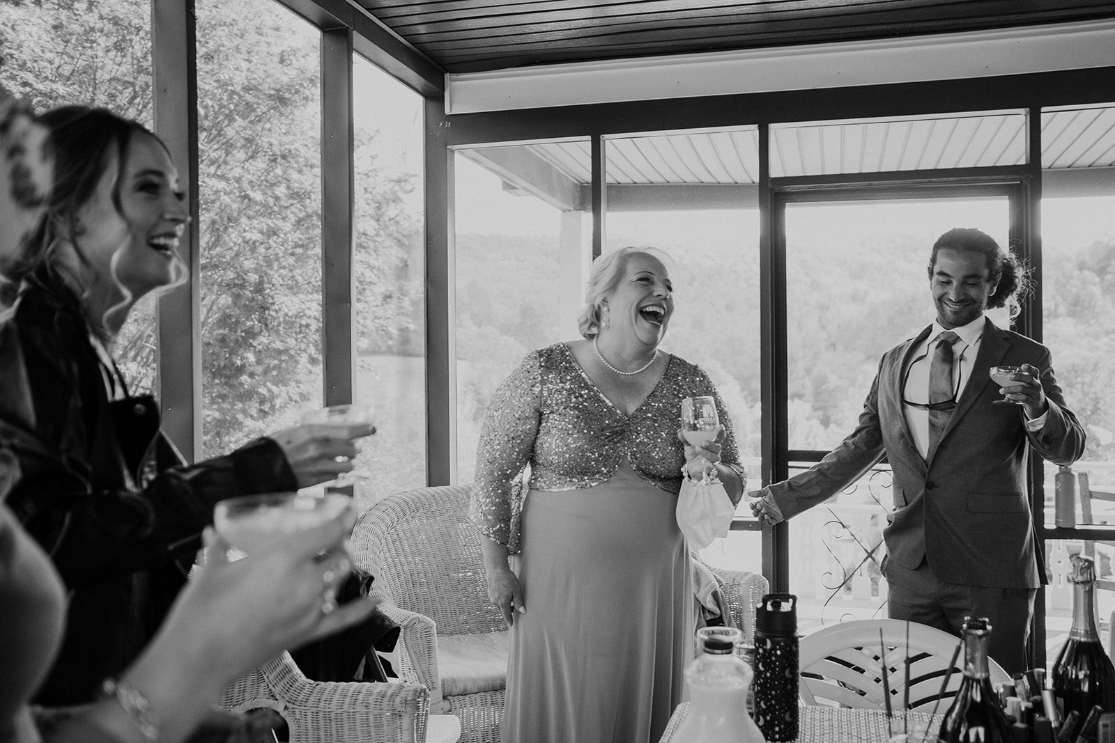 The mother of the groom laughs while drinking a mimosa as she prepares for her son's outdoor farm wedding ceremony.