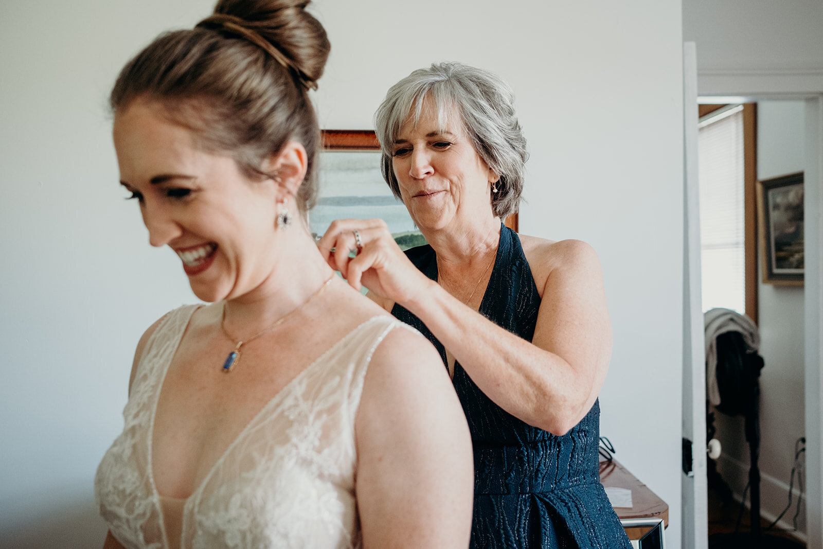 The mother of the bride helps her daughter put on her necklace on her wedding day. 