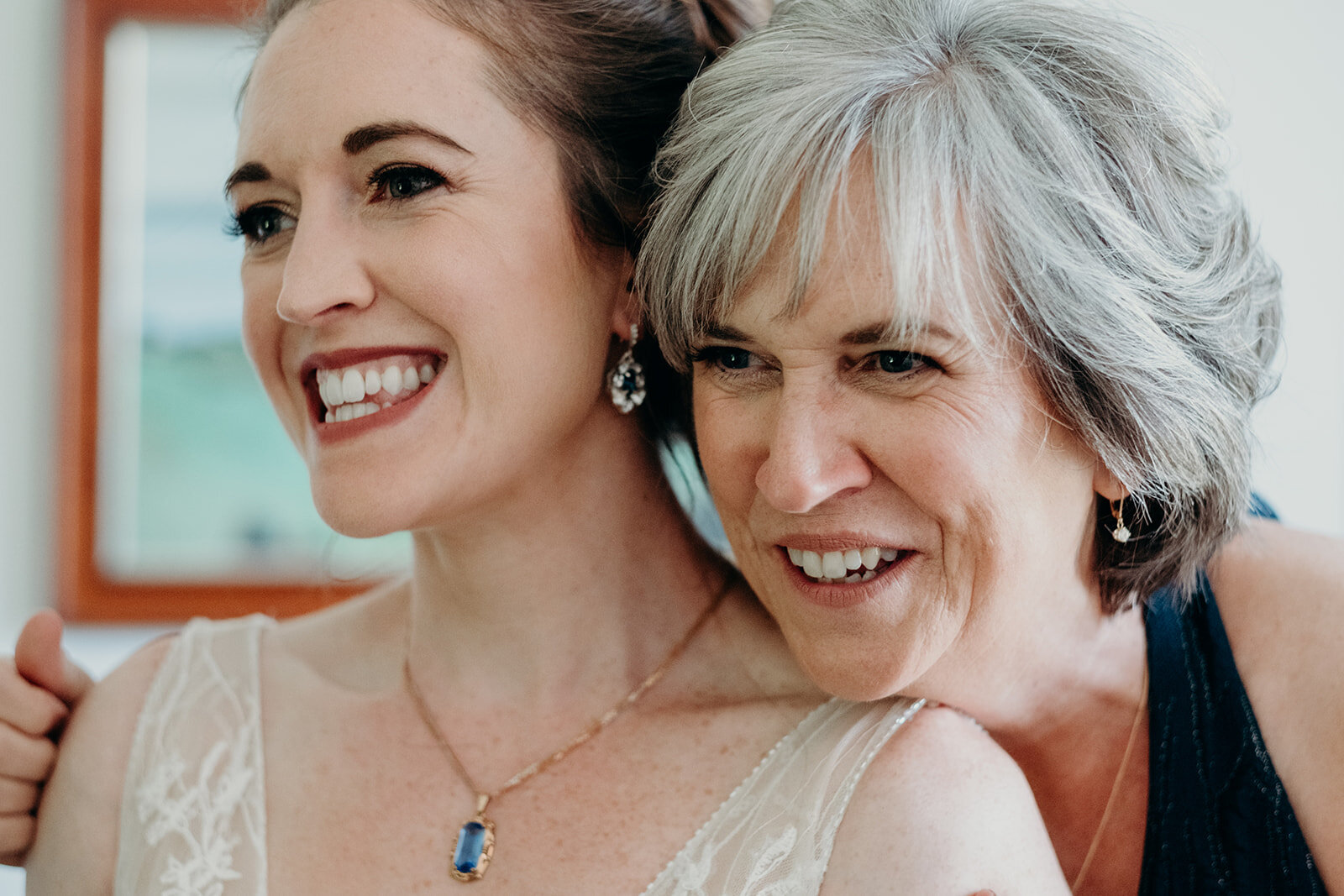 The mother of the bride gives her daughter a hug after placing on her necklace on her wedding day. 