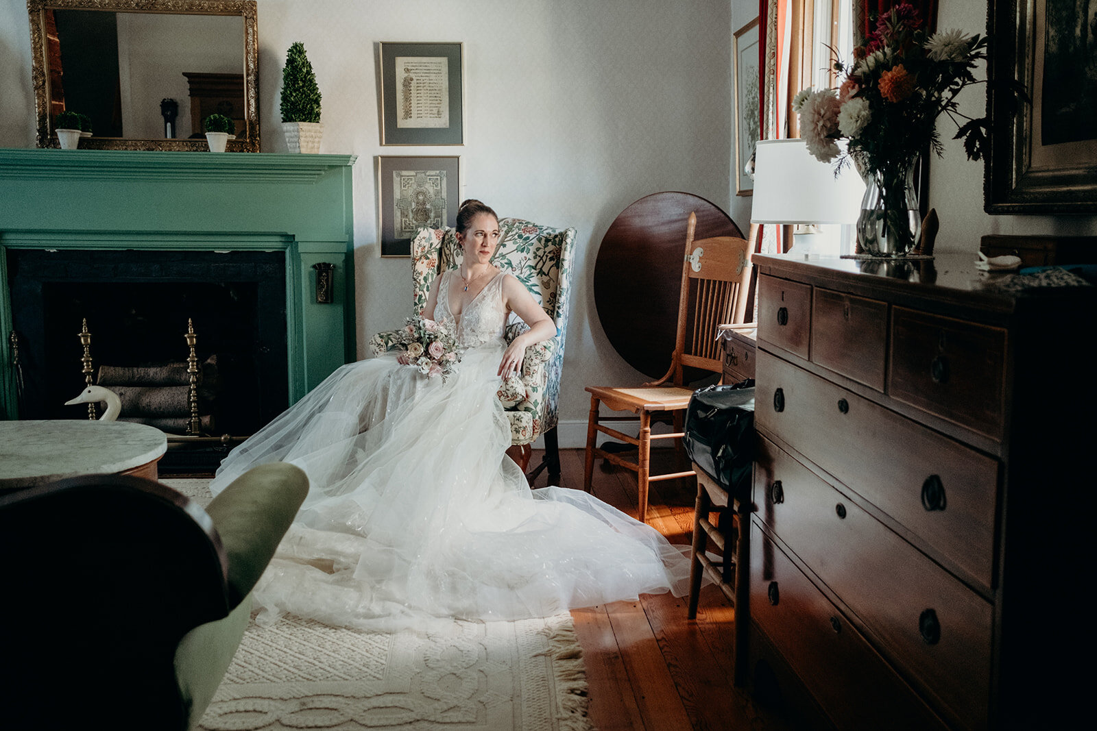 A bride sits in the living room of an old farmhouse and looks out the window before her outdoor wedding ceremony.