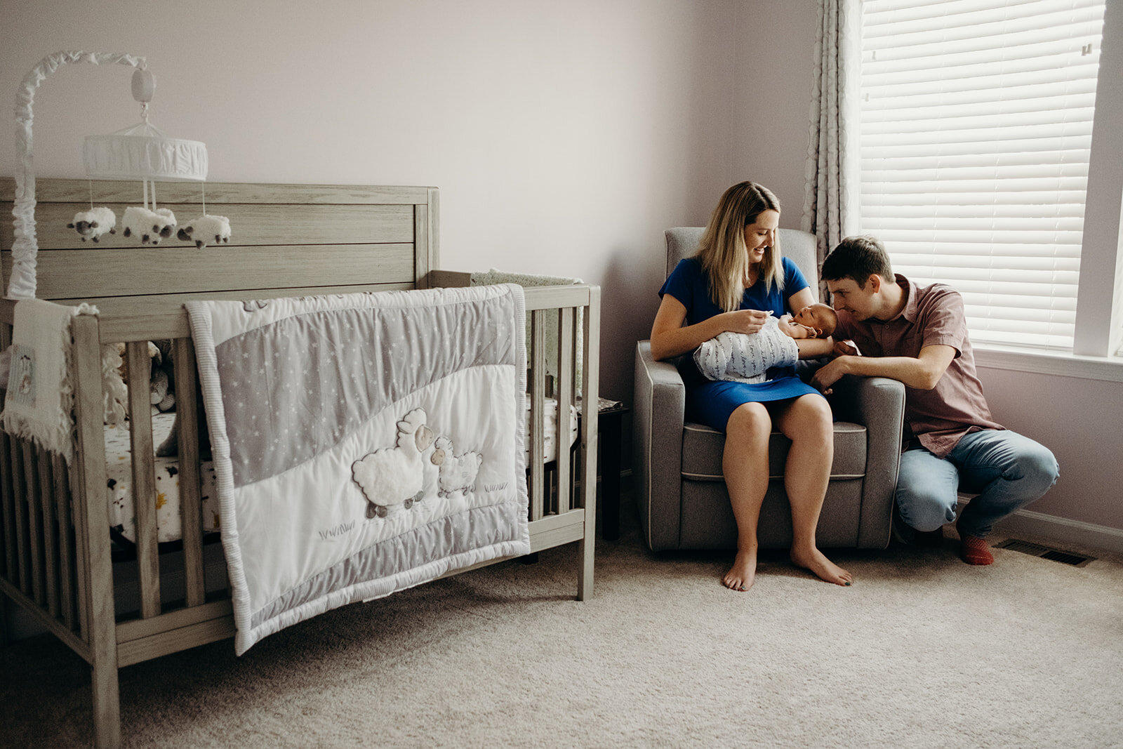 A mother and father snuggle their newborn baby in the nursery.