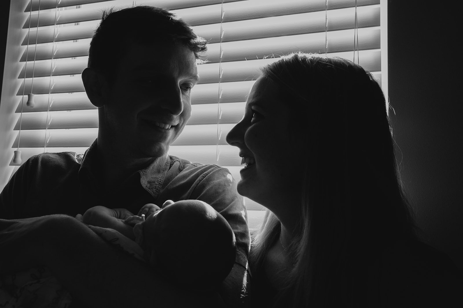 A mother smiles at her husband while he holds their newborn baby girl. 