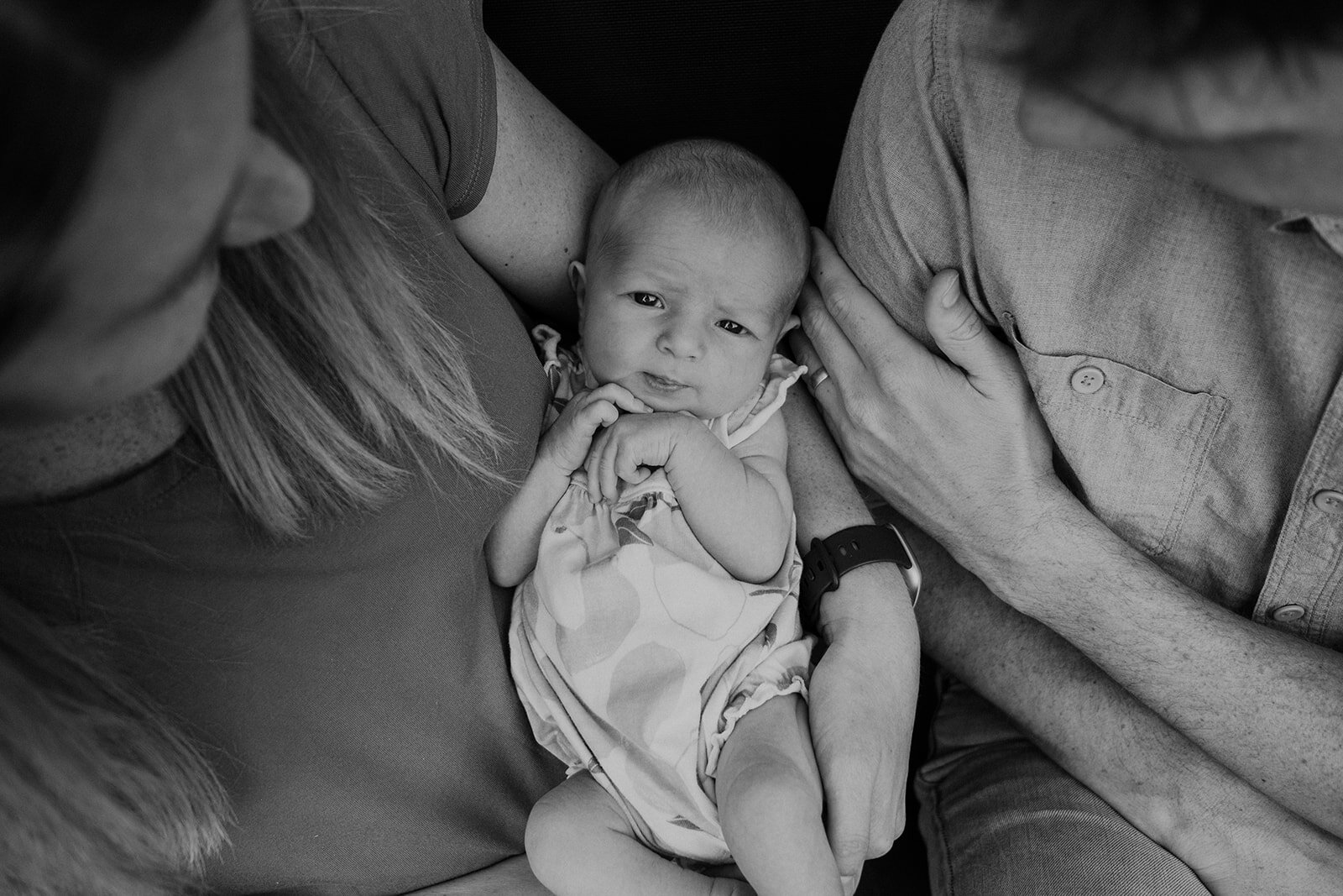 A newborn baby girl looks up at the camera while being held between her mother and father. 