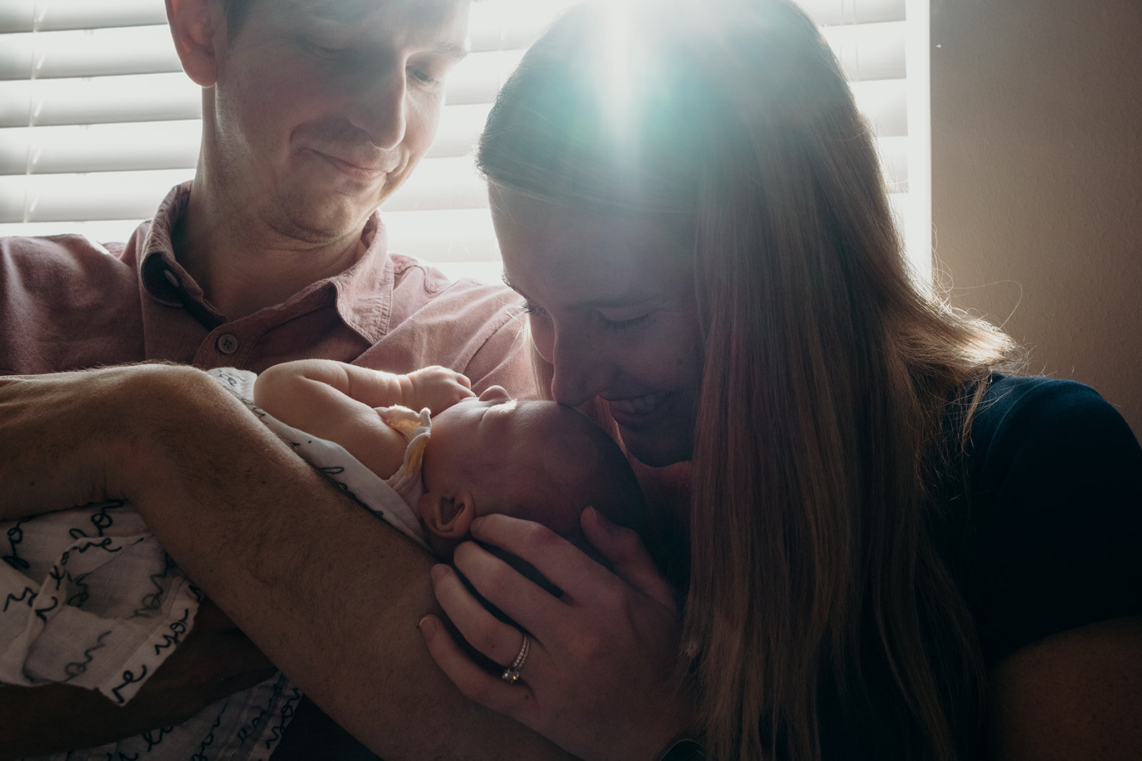 A mother kisses the forehead of her newborn daughter while her husband holds her.