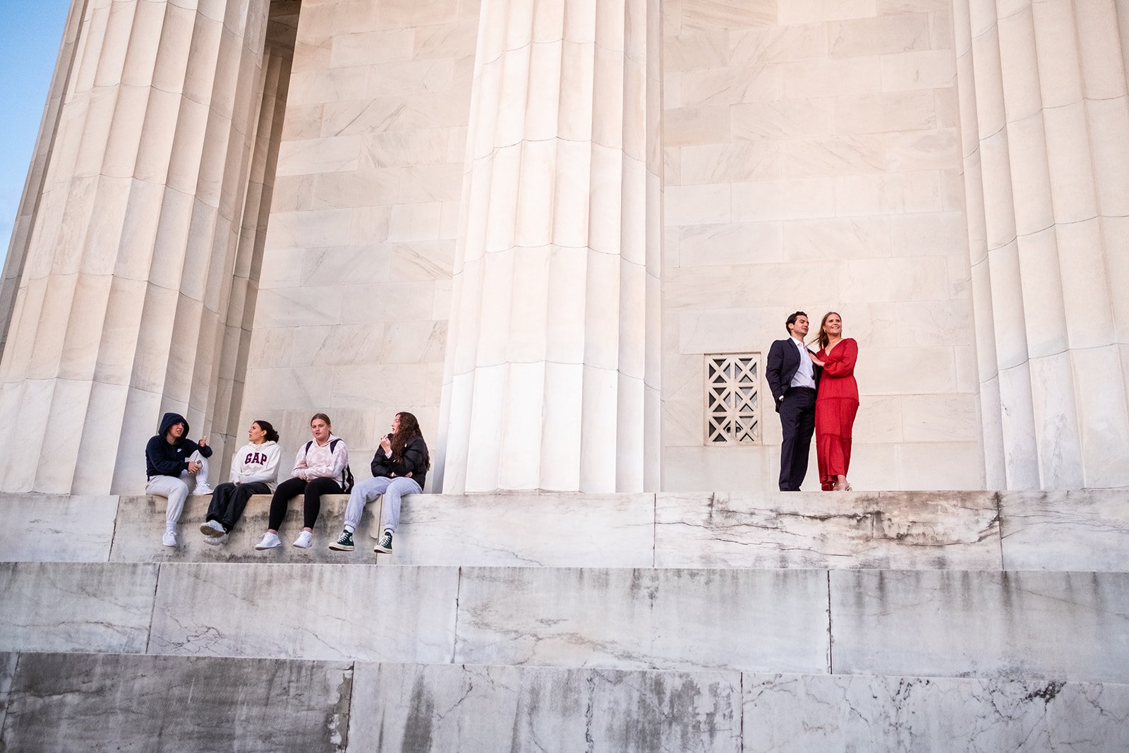 A group of tourists looks on at an engaged couple standing by the pillars at the Lincoln Memorial in Washington, DC. 
