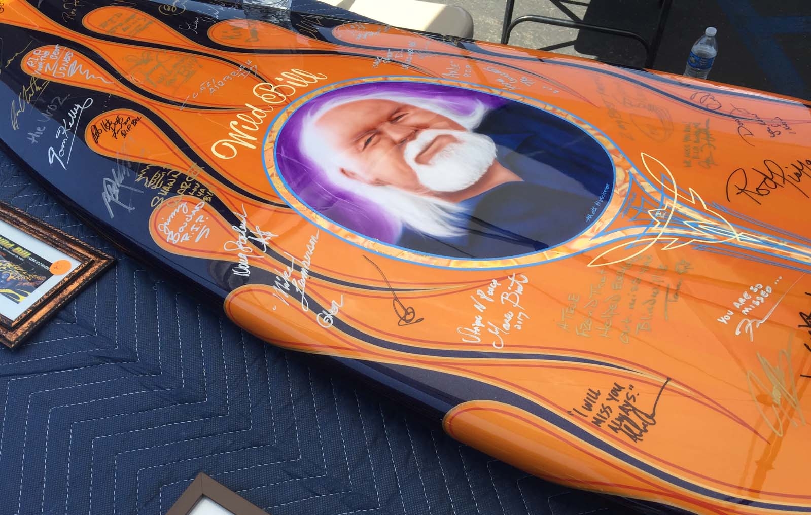 A restored surf board crafted by the late Wild Bill, sits on the display table at the Riverside Nationals Car Show. The surf board was retouched and painted by fellow pinstriper and painter, Herb Weber and rendering created by artist, Matt Hutchinson, to commemorate Wild Bill. The surf board has been taken to several car shows this Spring and signed by friends, pinstripers and family.