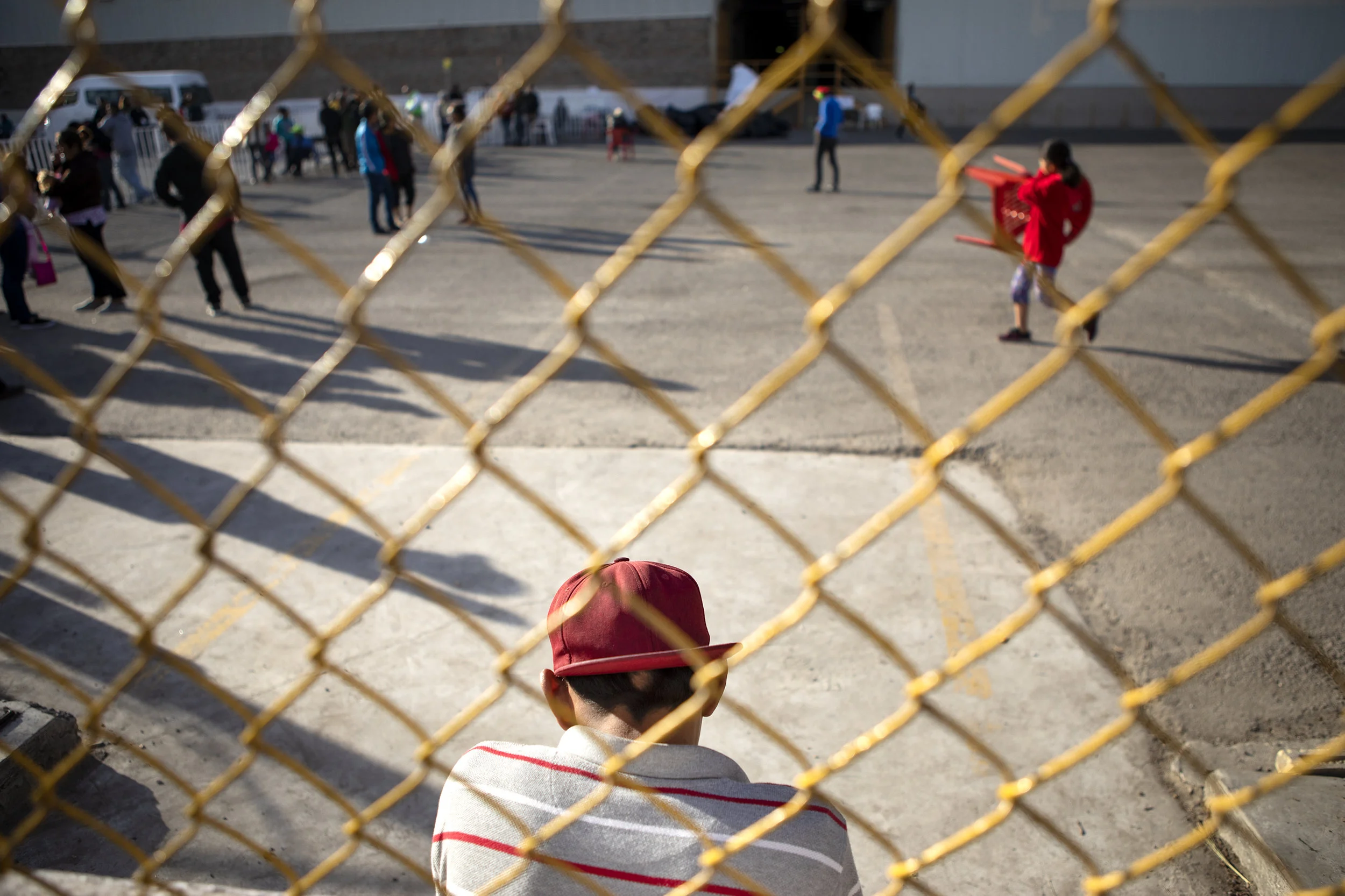 A young boy sits by the fence of the migrant shelter in Piedras Negras, Coahuila. There are an estimated 700 migrants remaining at the shelter. A decrease from 1700 migrants on Feb 4., 2019.The shelter is slated to close later this week. Feb. 18, 2019. Miguel Gutierrez Jr./The Texas Tribune