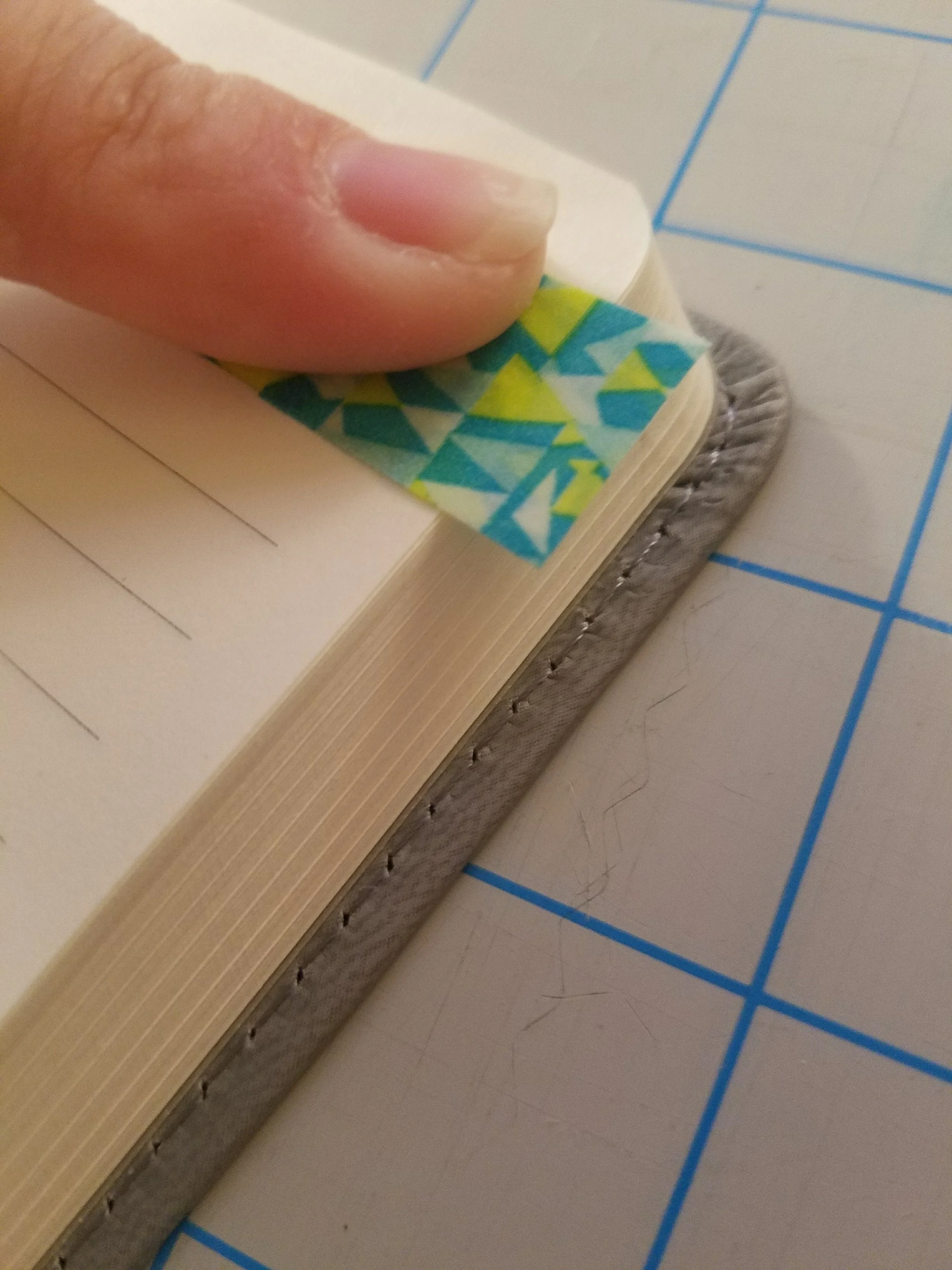 Take a piece of Washi tape approximately 1.5" long and fold about a 1/3 of it in half so that it sticks to itself. Then take the remaining sticky part and attach to the page. 