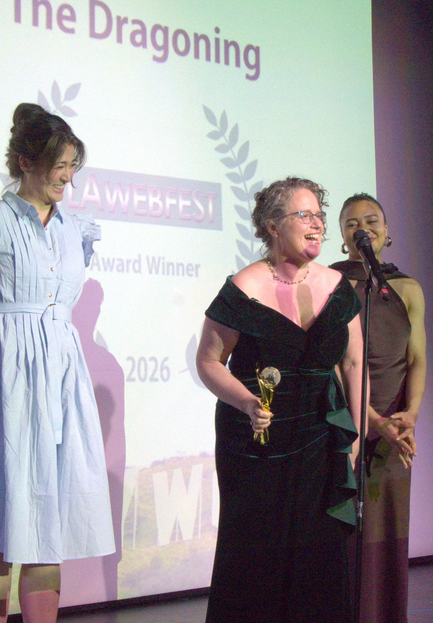 Emily Rainbow Davis holds the LA WebFest Award in front of Jacki Jing and Victoria Williams. The sign behind reads: The Dragoning LAWEBFEST Award Winner 2026