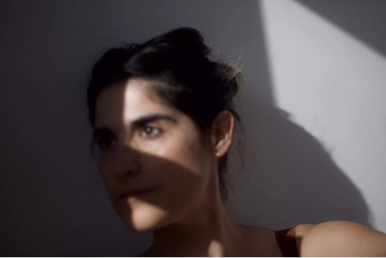 A woman with dark hair and earrings looking to the side, with sunlight casting a shadow across part of her face.