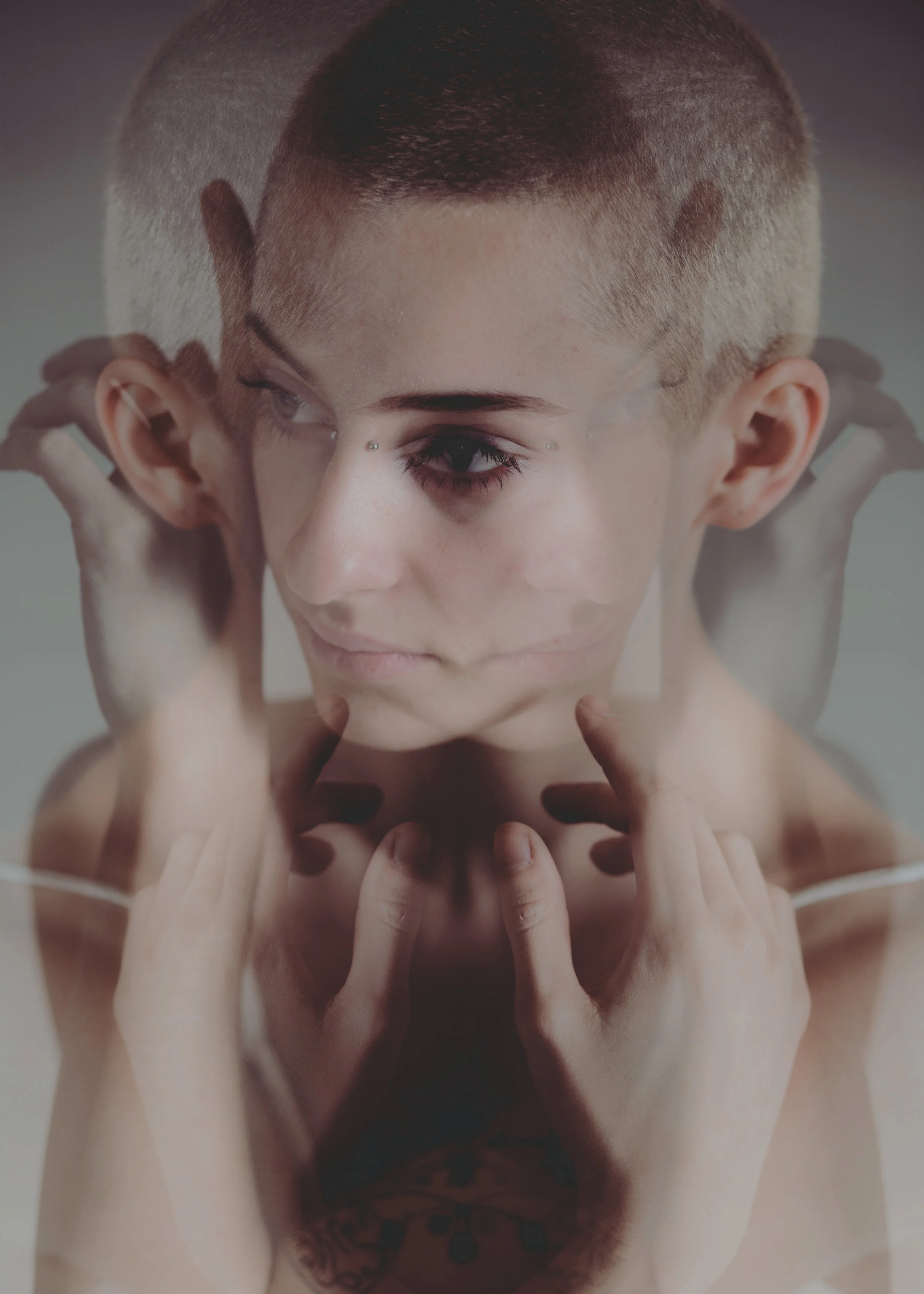 A person with a short, buzzed haircut and facial piercings, touching their face with multiple hands or fingers, with a focus on their eye and eyebrow.