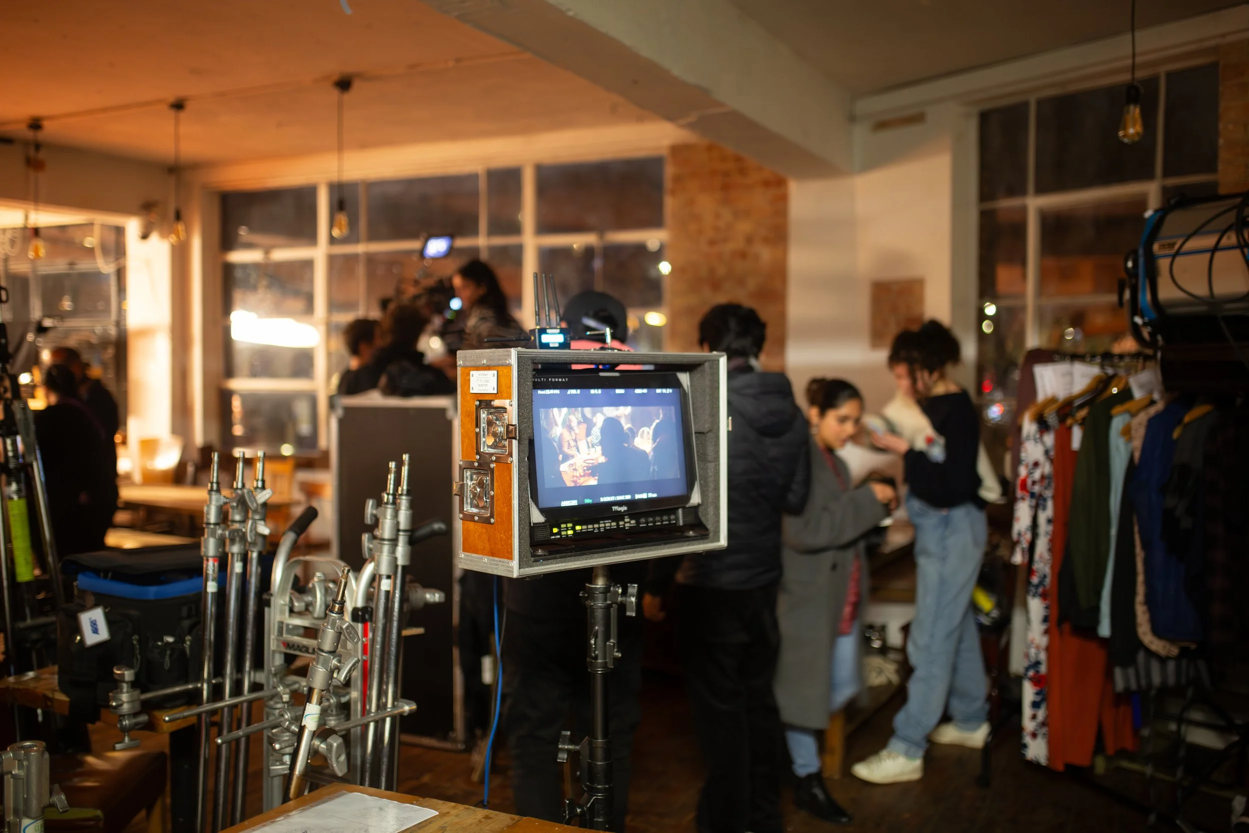 Indoor scene at a busy retail store with people shopping and a filming camera in the foreground.