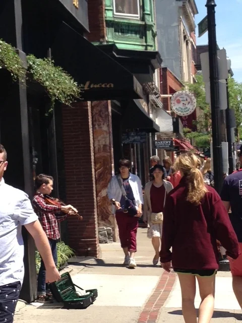 Streets are crowded with pedestrians. There are so many "eyes on the street" that residents tell us that they are never afraid even walking around at night. Notice the brick trail laying out the route of the Freedom Trail and the young man playing his violin for change. 