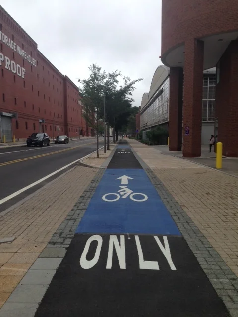 The right side of this brick lined elevated sidewalk is dedicated to pedestrians and the left side is for bicycles only. Same set-up for bikers and walkers is on the other side of the street. Note the presence of tree plantings on the street edge. Up further, I saw perennial plantings on the edge of the sidewalks towards the building fronts. The street here has two traffic lines in opposite directions and two lanes for parking. This street was at one time probably more like a speedway. Think Mill Street or Major Taylor Boulevard, Worcester! Look how a street can be converted to slow traffic and increase the access for bikers and walkers so that the street becomes a public way! 