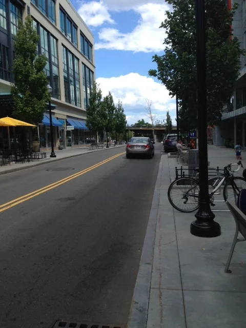 This is Artisan Way, the main drag in this two T-shaped street village. Note the wide sidewalks, the benches, the street trees and plantings, the old fashioned street lamps.... all making this a walking friendly place. Bikers are welcomed here too. There are plenty of bike racks scattered throughout the development and street markings designating bicycle passages. Bikers and walkers are free to enjoy the path along the Mystic River. The streets in this development (see in photo) are human scaled with just one narrow lane in either direction. Cars are allowed to park in metered spaces on the street on the right side. This is a good example of a "complete street" where cars, bicyclists and walkers have equitable access to the road space.