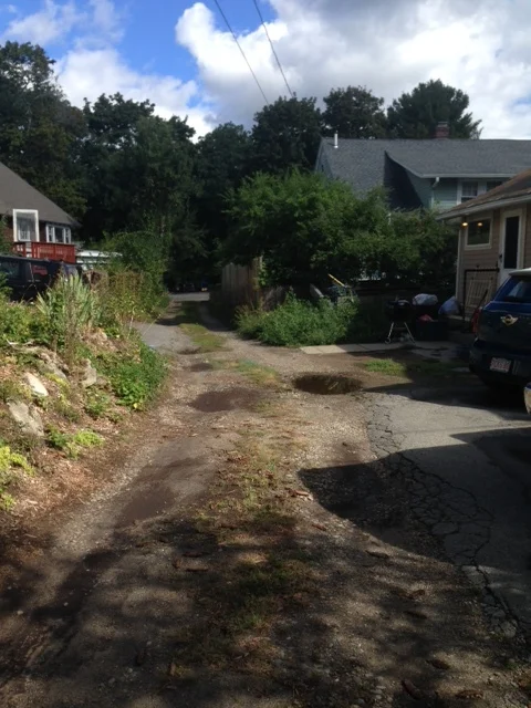 Unpaved narrow alleyway provides access to parking spaces for cars BEHIND THE HOUSES not in the front.
