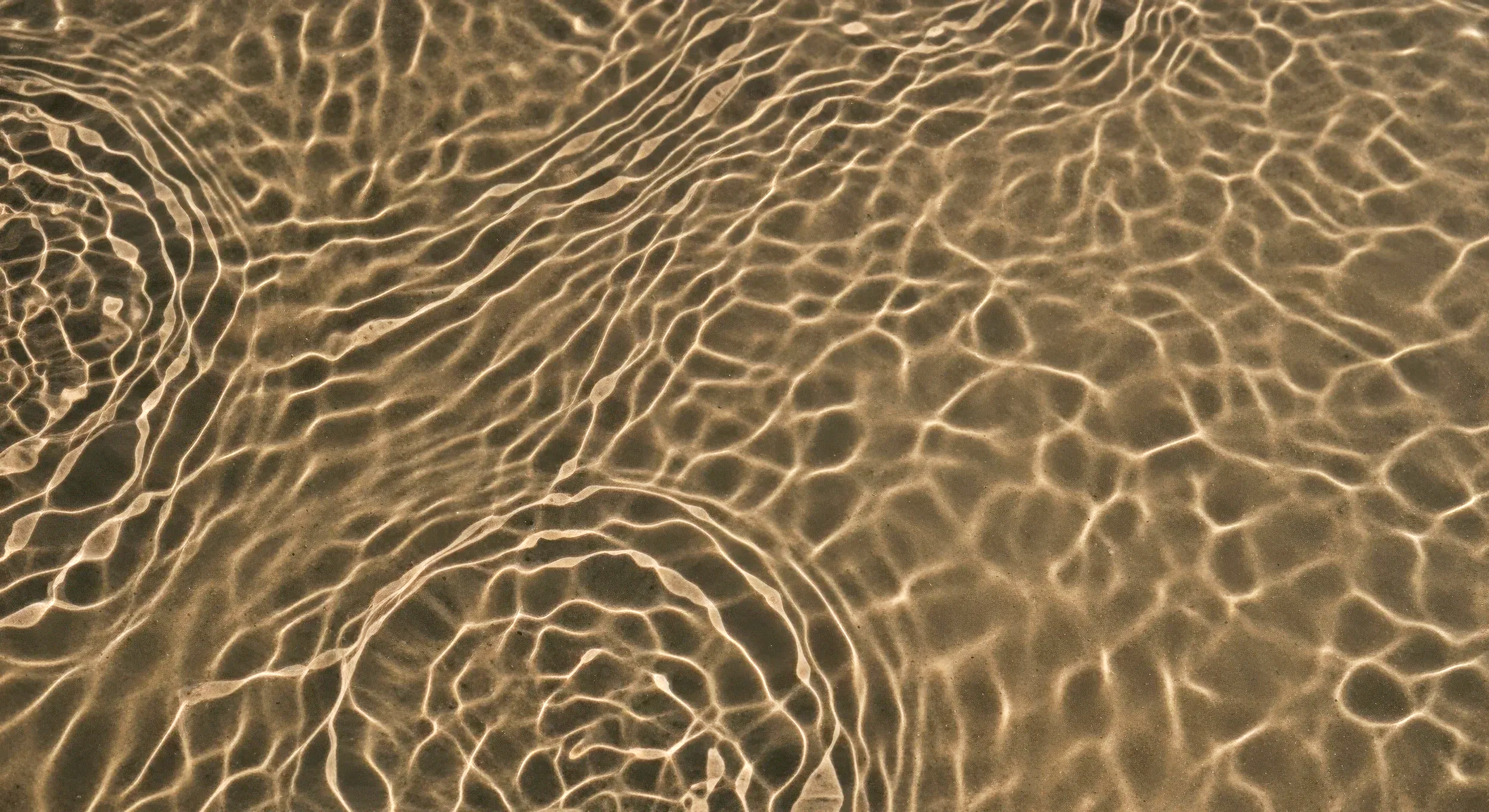 Close-up of water with sunlight reflections creating intricate ripple patterns.