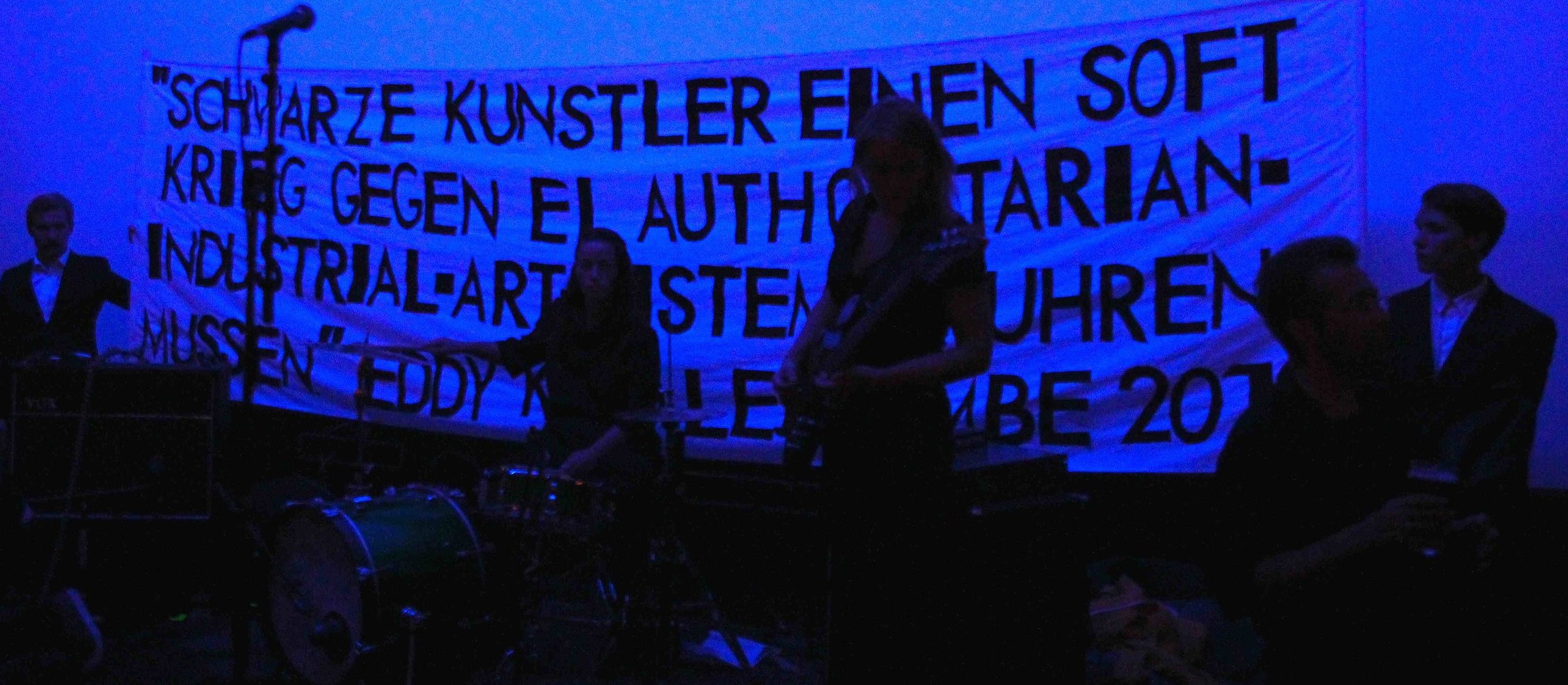 Our Literal Speed presents "Our Literal Speed," dimensions variable, materials: all-female band playing the main riff from "Kashmir" again and again, male models, LGBTQ rights "propaganda" banner rendered in art world lingua franca, two-person lecture, 29 August 2013, Bergen Kunsthall, Bergen, Norway (detail)