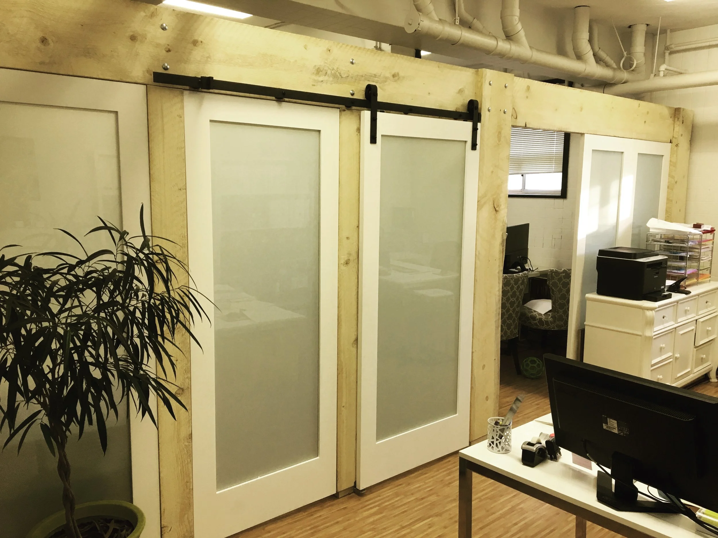  Partition wall with sliding bard door. Rough sawn beam with frosted glass doors and panels. It gives the office a meeting room but still feels bright and open.  