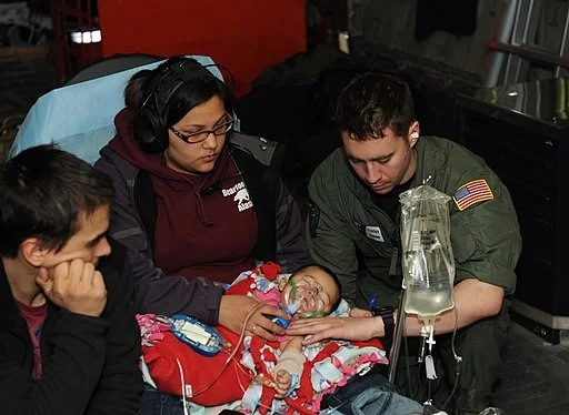 KODIAK, Alaska - Coast Guard Petty Officer 3rd Class David Call, a health services technician with Rockmore-King Clinic and resident of Ridgefield, Wash., counts a 5-month-old girl's breath respirations during a medevac aboard an HC-130 Hercules air…