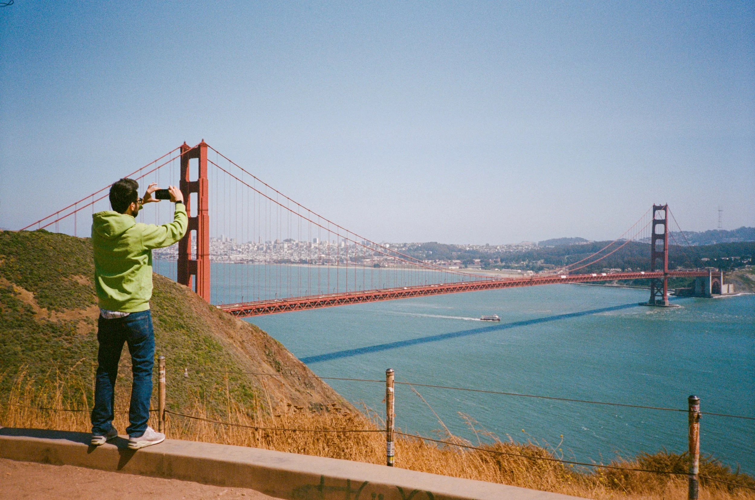 Man standing taking a photo of the Golden Gate Bridge.
