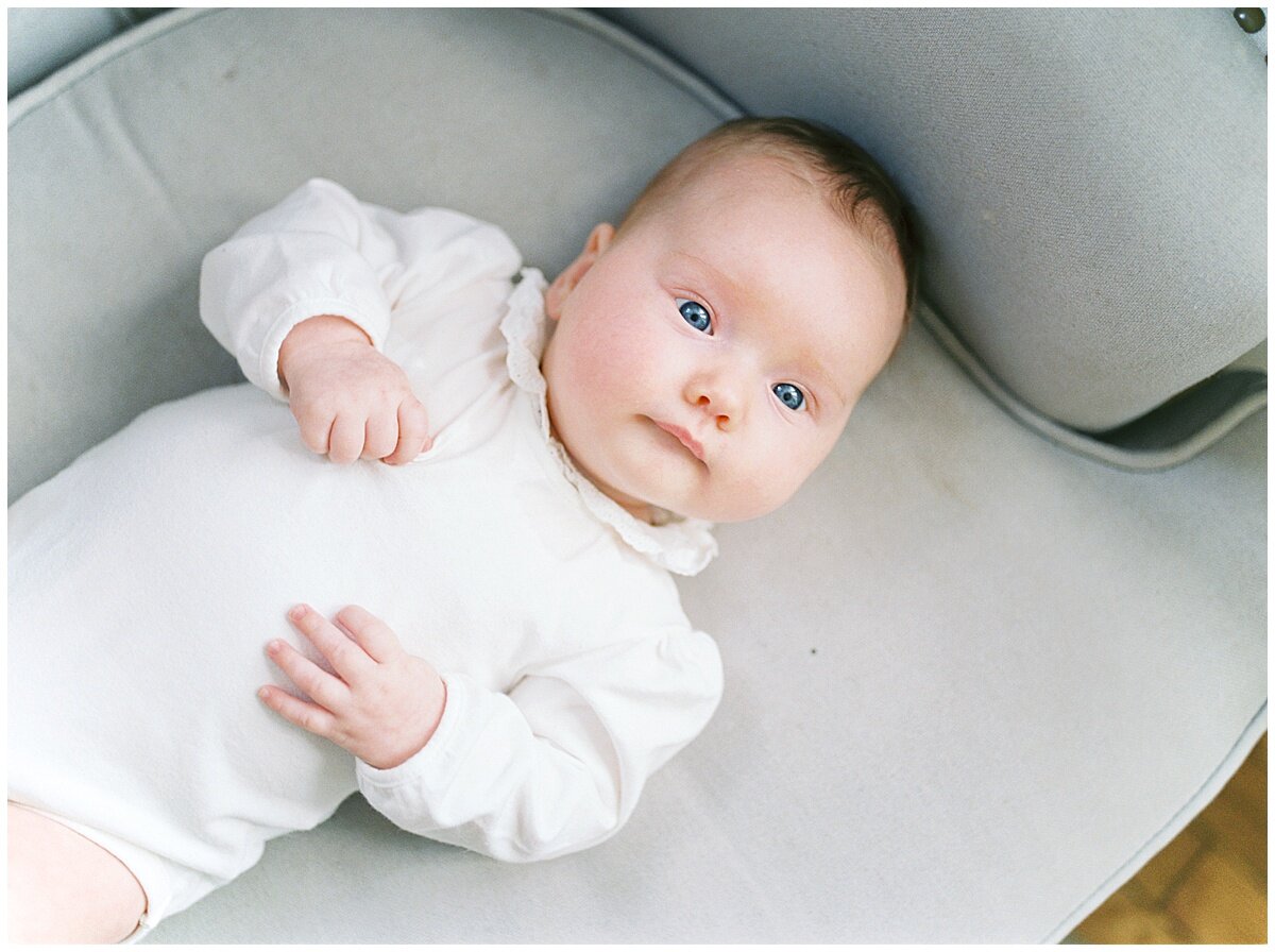 Blue-eyed baby laying on gray chair during a COVID photography project.