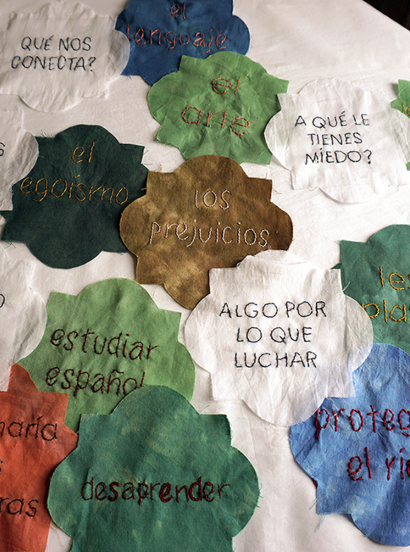 Velasco_Spaces of Conviviality_fabric, embroidery_2018_73 L x 26 W in/Centro Negra-AADK, Murcia, Spain. Participatory Art Project working with the community around concepts of migration, displacement, identity and integration. I created a ‘game’ which invited residents to share personal stories through conversation. These stories served to construct an “identity flag”, which was hand-embroidered by community members and unveiled as a public art event during Open Studios.