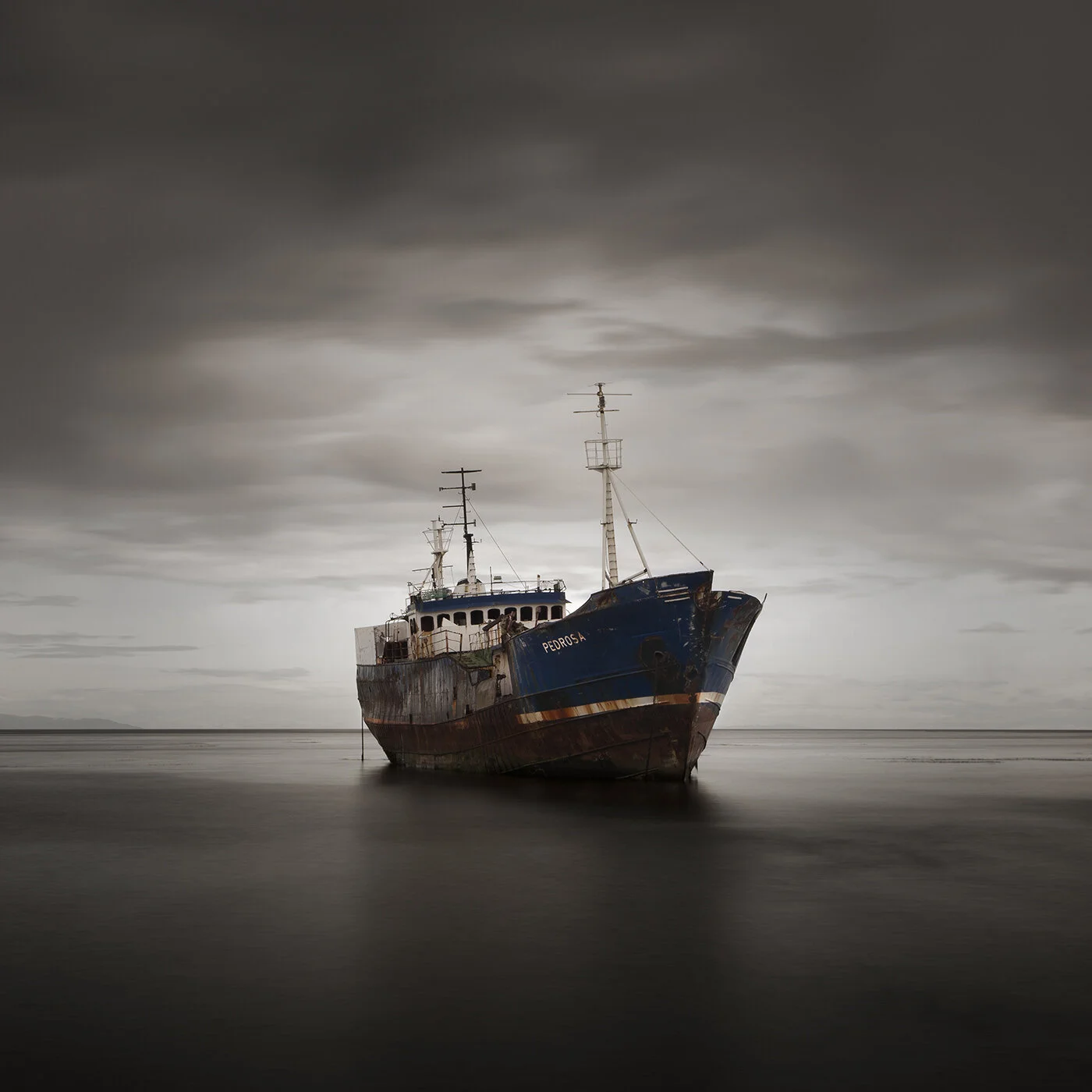 A rusty, solitary ship named Pedrosa stranded in shallow water under a cloudy sky.