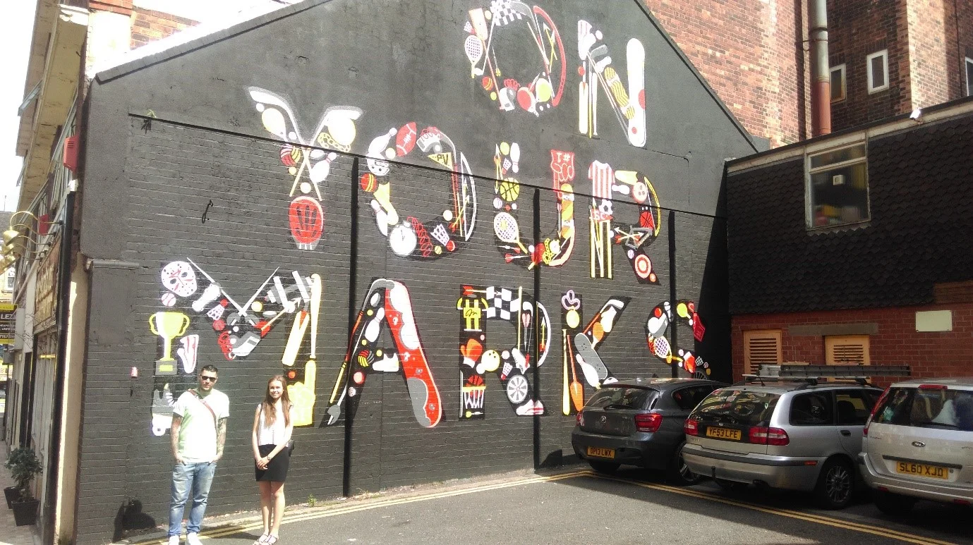 En route to 'Entrepreneur' - Andy and Becky by his City of Sport mural off Cheapside